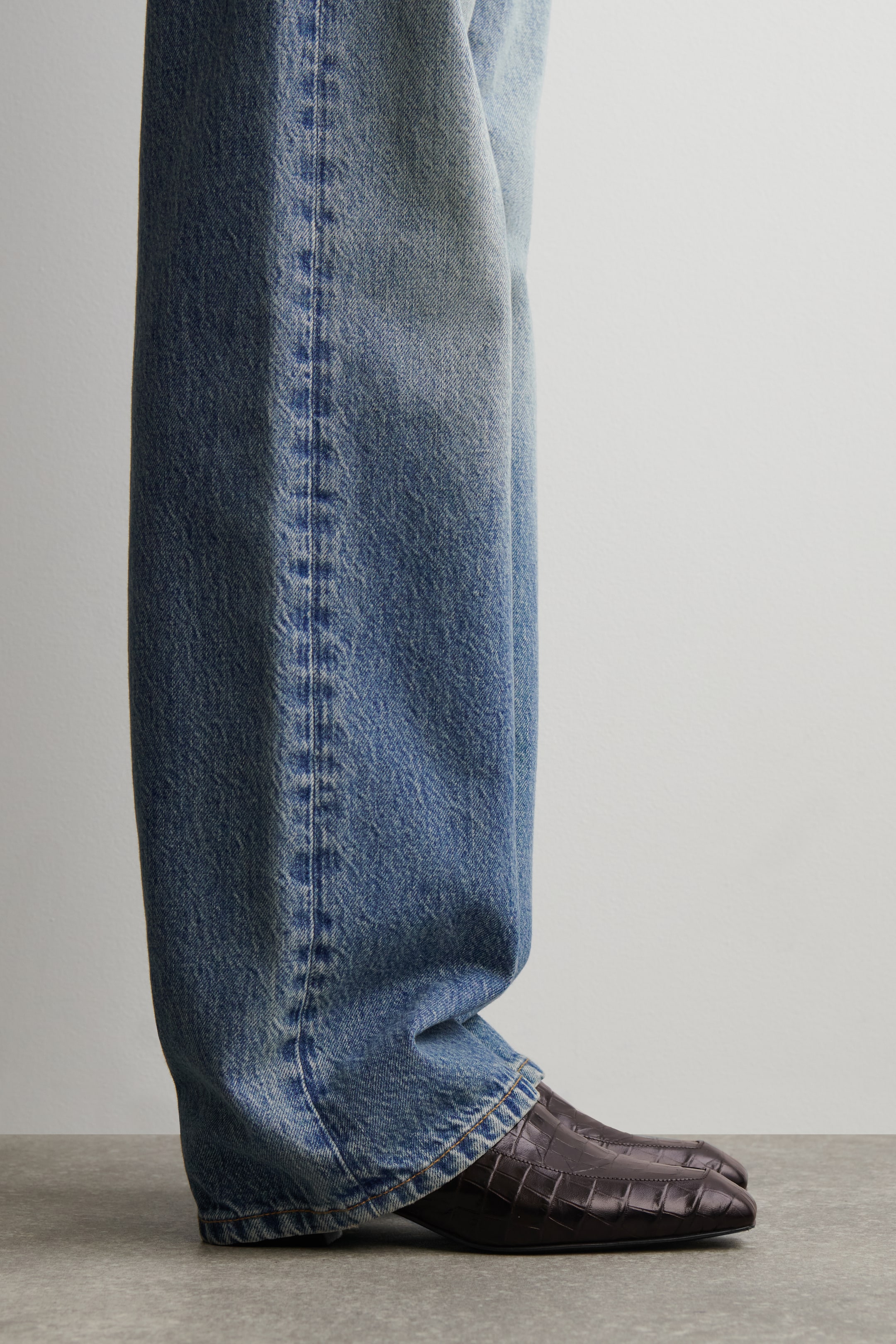 Agrandir l'image: Des chaussures à bout carré en cuir marron foncé embossé crocodile sont portées, vues sous un angle de côté-avant. Un jean bleu clair à jambes larges couvre la partie supérieure des chaussures.