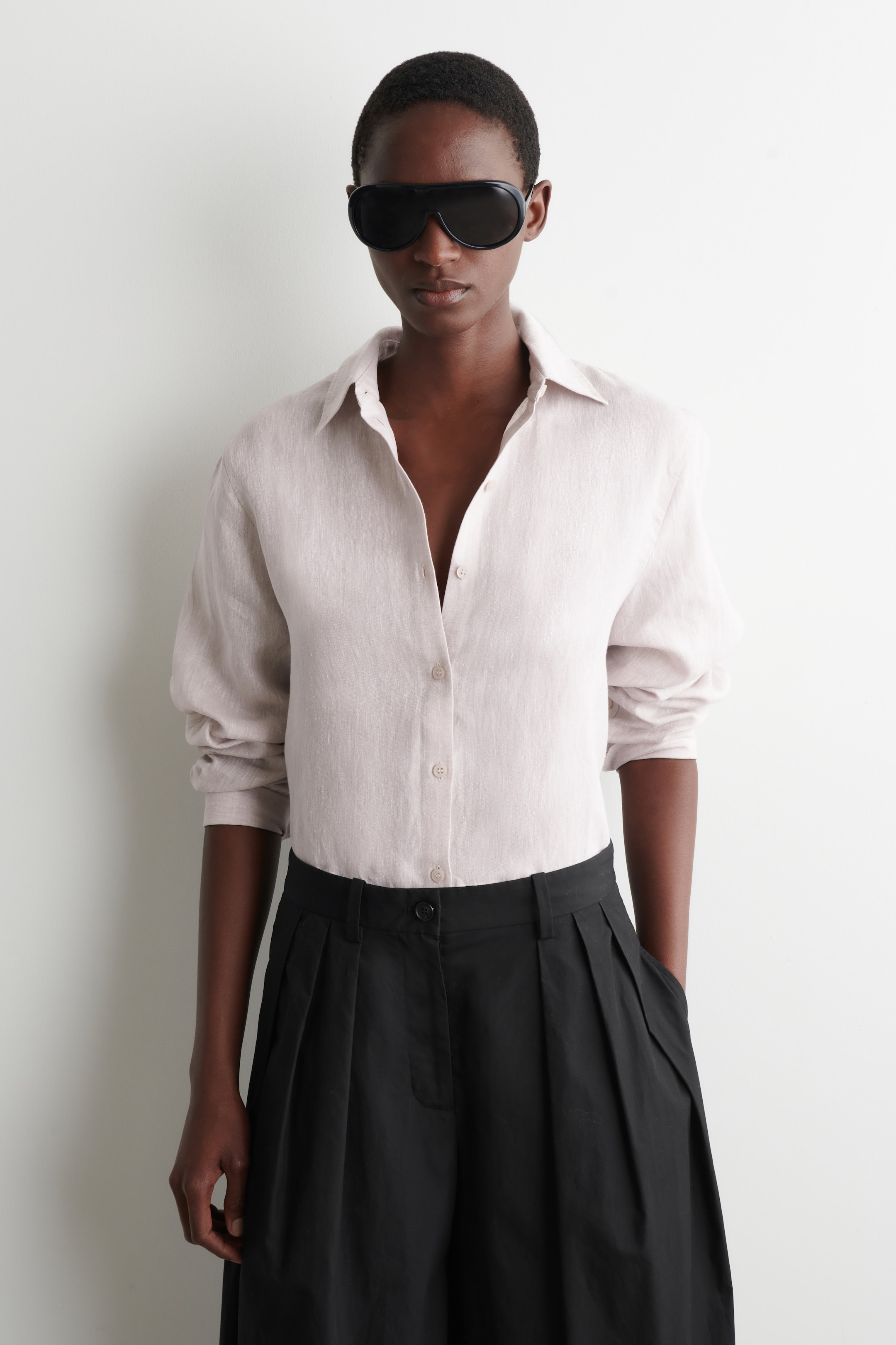 הצגת תמונה גדולה יותר: חולצת פשתן בצבע בז' בהיר כוללת צווארון קלאסי ושרוולים ארוכים מעט נפוחים, המורמים באזור השרוול. היא מוצגת עם חזית כלפי מעלה, מכופתרת בחזית ומוכנסת לתוך מכנסיים שחורים.