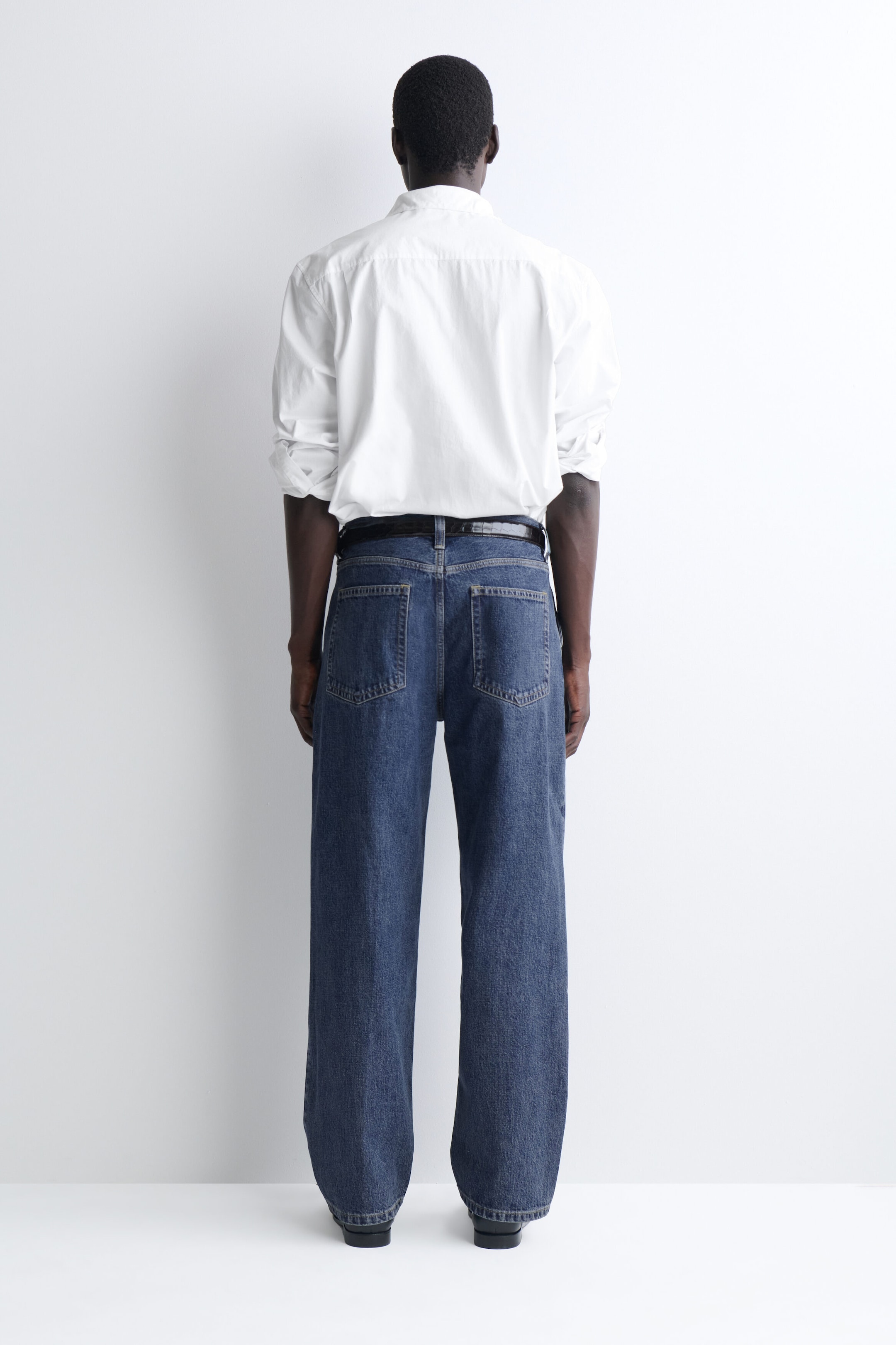 These relaxed-fit, straight-leg denim trousers are shown from the back, highlighting their classic rear patch pockets and straight silhouette in a medium blue wash. The trousers are styled with a tucked-in white shirt and a dark leather belt to emphasise the mid-rise waistband. These relaxed-fit, straight-leg denim trousers are shown from the back, highlighting their classic rear patch pockets and straight silhouette in a medium blue wash. The trousers are styled with a tucked-in white shirt and a dark leather belt to emphasise the mid-rise waistband.