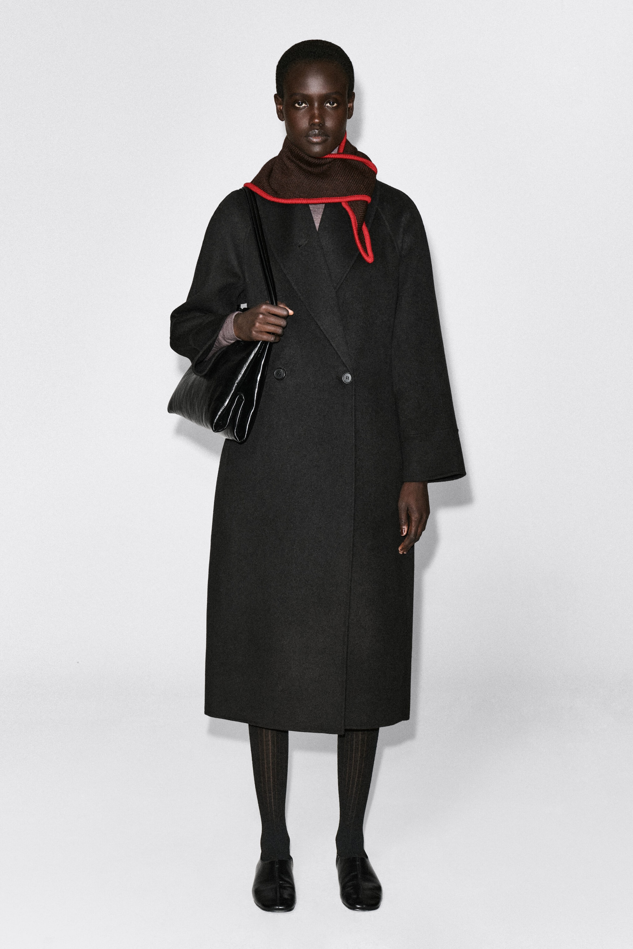 L’écharpe triangle en laine mérinos à pointes contrastantes, de couleur marron foncé, est enroulée autour du cou d’un mannequin de face, portée par-dessus un long manteau noir à double boutonnage. L’écharpe met en valeur une bordure contrastante rouge vif le long de ses bords en maille. L’écharpe triangle en laine mérinos à pointes contrastantes, de couleur marron foncé, est enroulée autour du cou d’un mannequin de face, portée par-dessus un long manteau noir à double boutonnage. L’écharpe met en valeur une bordure contrastante rouge vif le long de ses bords en maille.