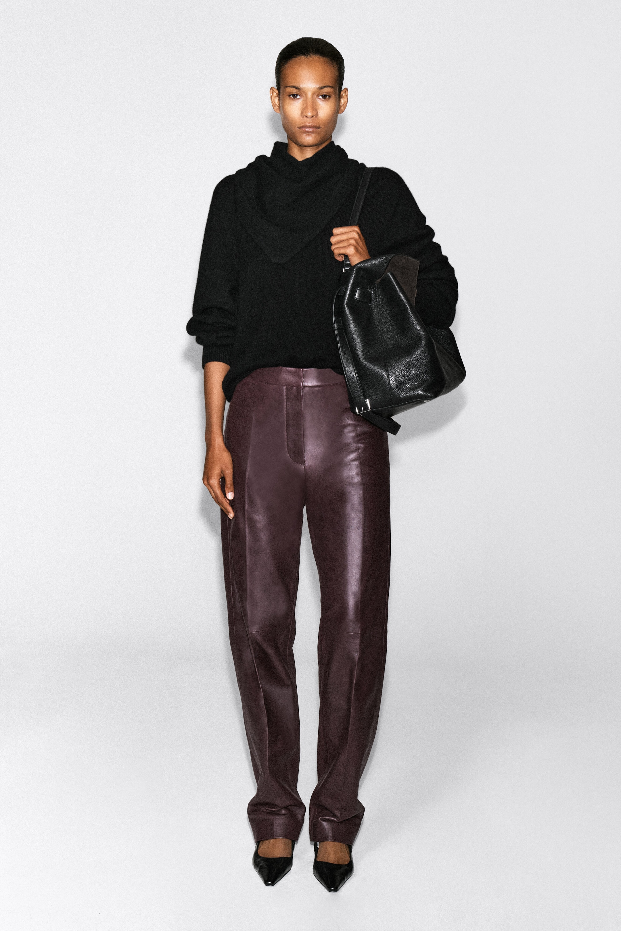 Leather straight-leg pants in a deep burgundy hue are worn by the model, featuring a high-rise waist, structured front creases, and a relaxed silhouette. The pants are styled with a black high-neck knit sweater and black pointed-toe shoes. Leather straight-leg pants in a deep burgundy hue are worn by the model, featuring a high-rise waist, structured front creases, and a relaxed silhouette. The pants are styled with a black high-neck knit sweater and black pointed-toe shoes.
