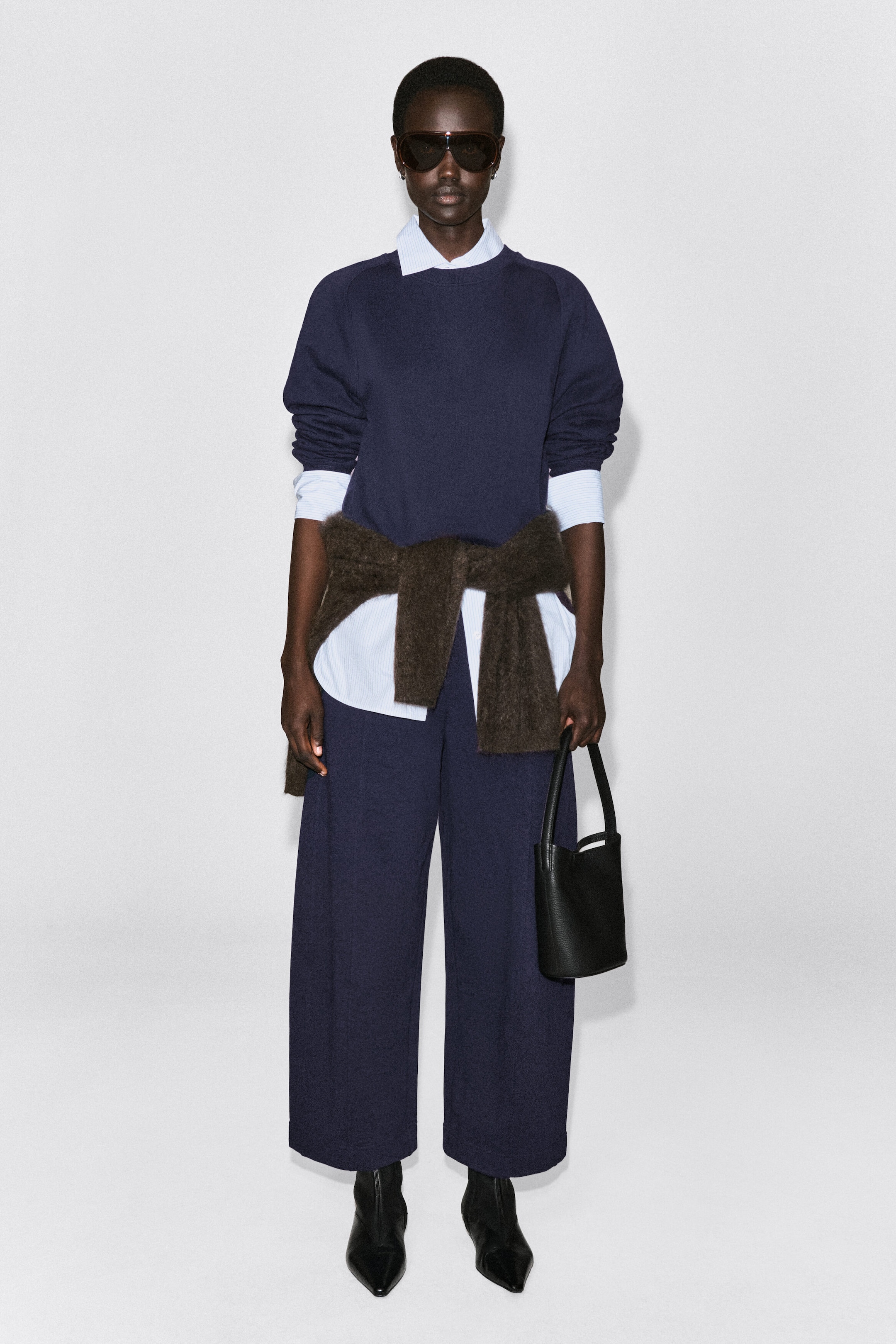A navy blue cotton sweatshirt is shown from the front, featuring a crew neck and relaxed-fit long sleeves. The sweatshirt is layered over a light blue striped collared shirt, with the collar and cuffs visibly extending past the neckline and sleeves. A navy blue cotton sweatshirt is shown from the front, featuring a crew neck and relaxed-fit long sleeves. The sweatshirt is layered over a light blue striped collared shirt, with the collar and cuffs visibly extending past the neckline and sleeves.