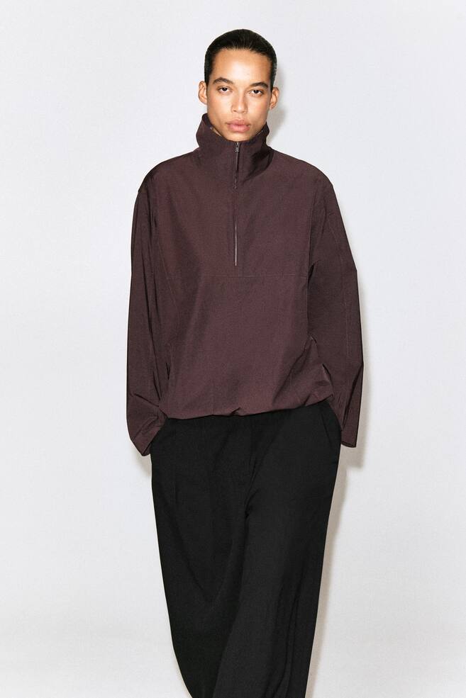 Een donker pruimkleurig half-zip pullover shirt wordt van voren getoond, met een hoge opstaande kraag met een zilverkleurige rits, lange mouwen en een geplooide zoom met trekkoord. - 1