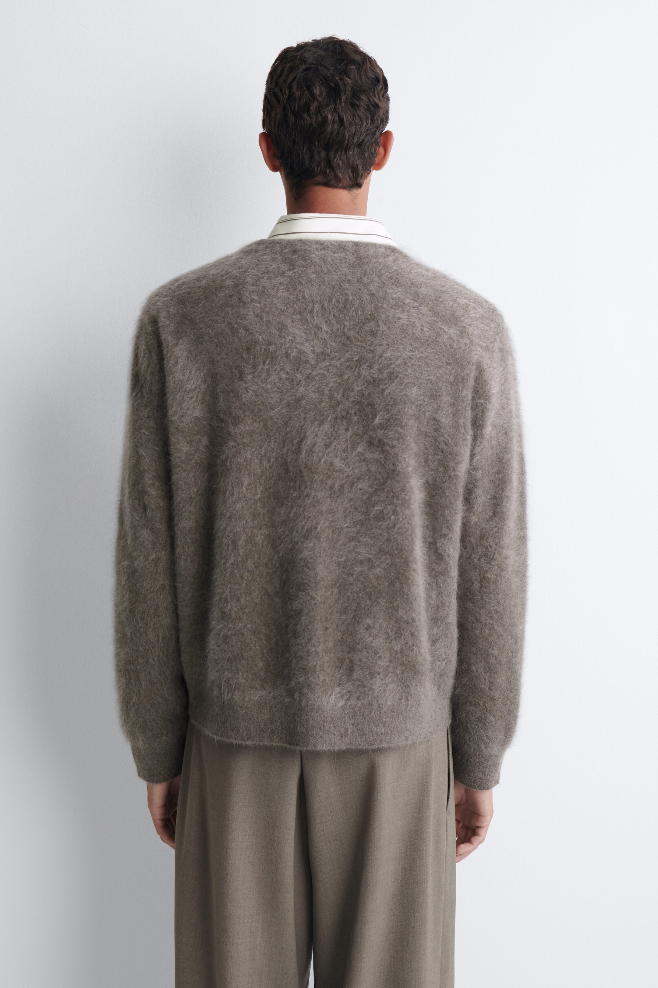 Un cardigan en cachemire brossé, dans une maille taupe duveteuse et texturée, est porté par le mannequin, présenté de dos. Le cardigan présente un ourlet et des poignets côtelés et est superposé à une chemise rayée à col, agencé avec un pantalon vert olive-gris. Un cardigan en cachemire brossé, dans une maille taupe duveteuse et texturée, est porté par le mannequin, présenté de dos. Le cardigan présente un ourlet et des poignets côtelés et est superposé à une chemise rayée à col, agencé avec un pantalon vert olive-gris.