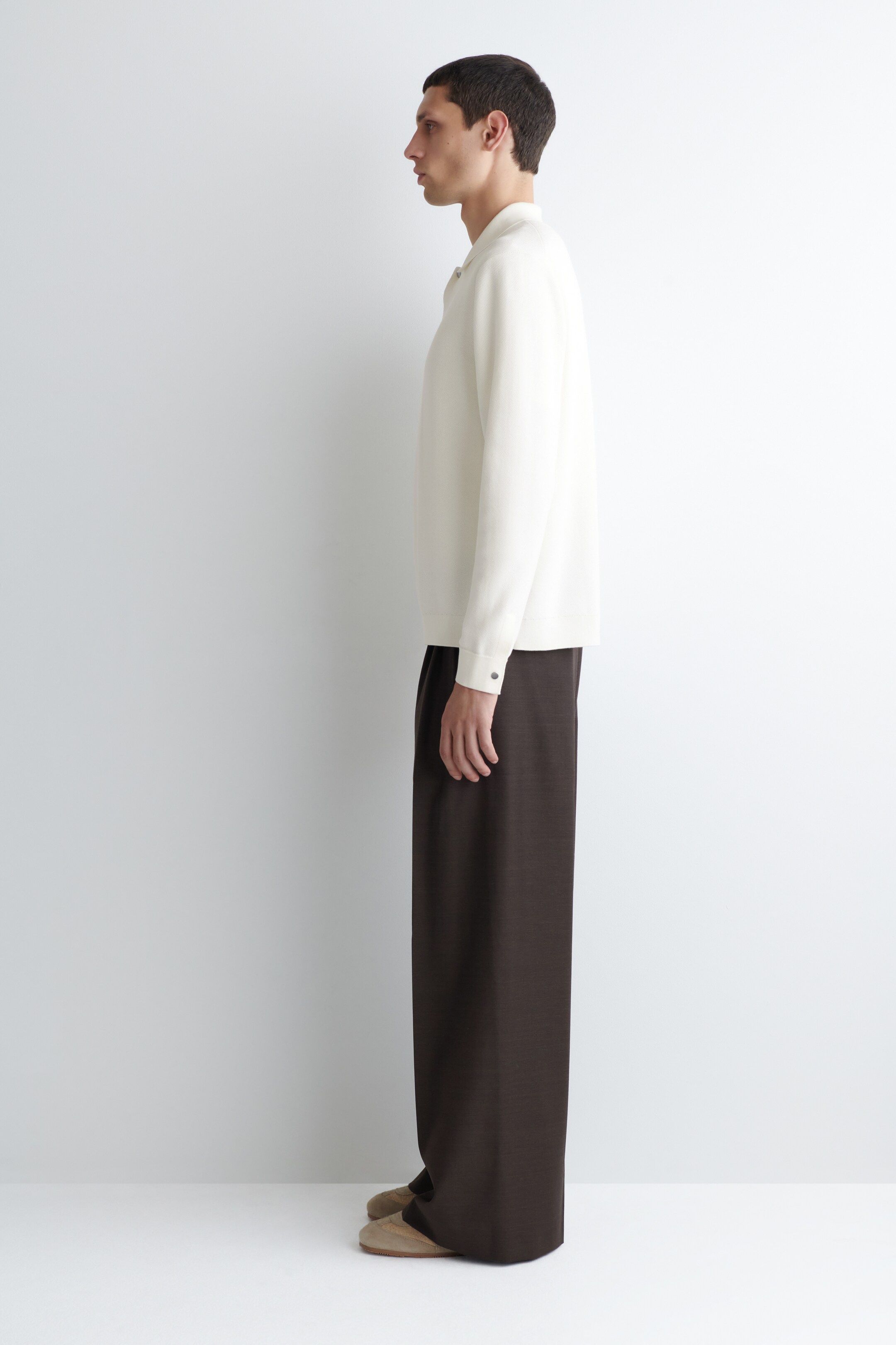View larger image: A cream-colored, long-sleeved knit polo shirt is being worn, featuring a spread collar and buttoned cuffs, and presenting a relaxed fit. Dark brown wide-leg trousers are also being worn, flowing loosely to the floor, with both garments viewed from the side.
