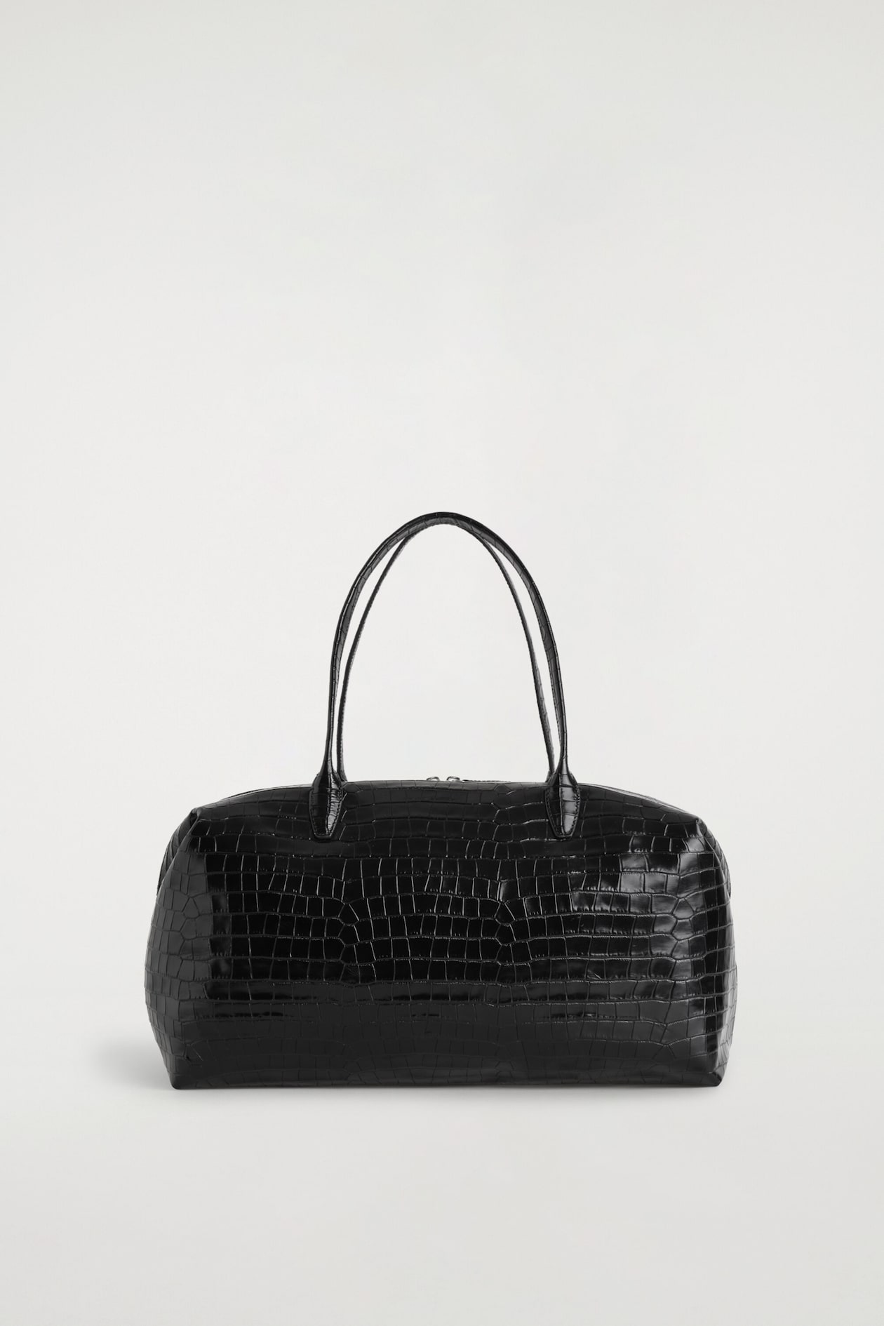 The Frieze bowling bag in black croc-effect leather is shown from the front, showcasing its structured rectangular silhouette and glossy embossed texture. Two slim arched top handles extend upwards from the main body of the bag.
