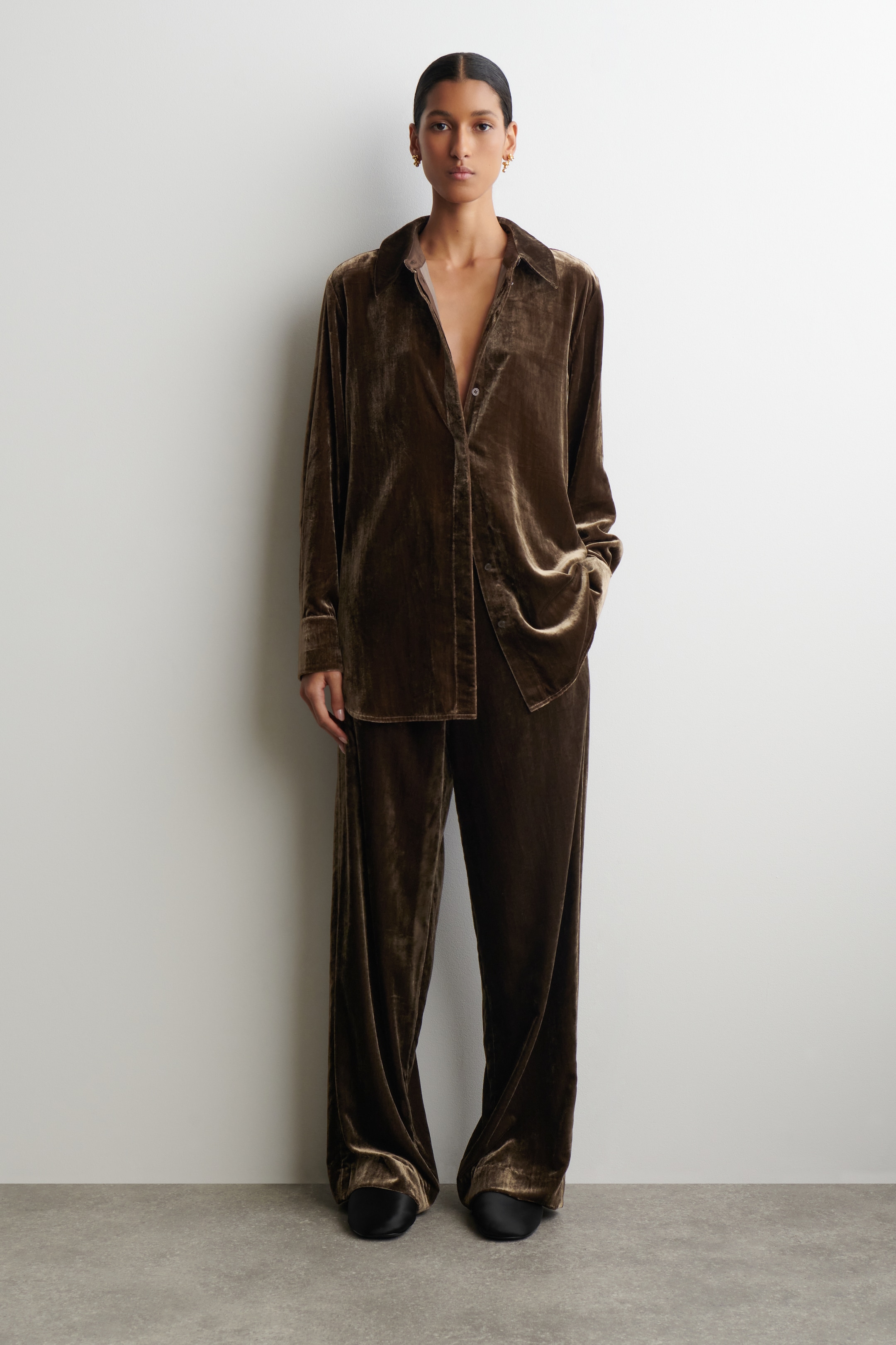 View larger image: A front-facing, dark brown lustrous velvet two-piece set is being presented. It features a loose-fitting, long-sleeved shirt with a collar and an open button-front, paired with wide-leg, full-length pants.