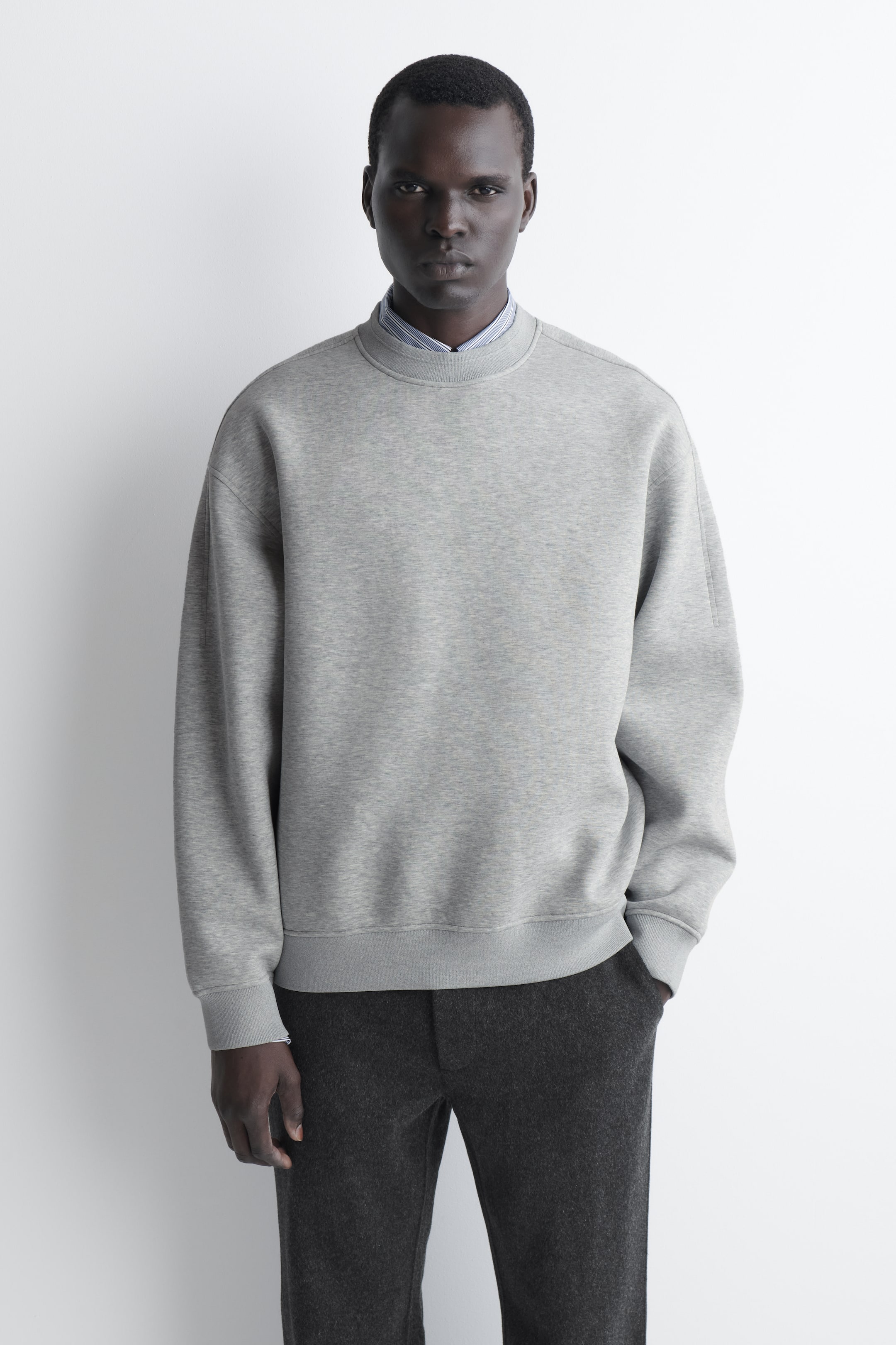 Agrandir l'image: Le sweat-shirt scuba coupe décontractée en gris clair présente, vu de face, une coupe ample avec épaules tombantes, poignets côtelés et ourlet côtelé. Un col de chemise à rayures dépasse subtilement sous l’encolure ronde, illustrant un style superposé.