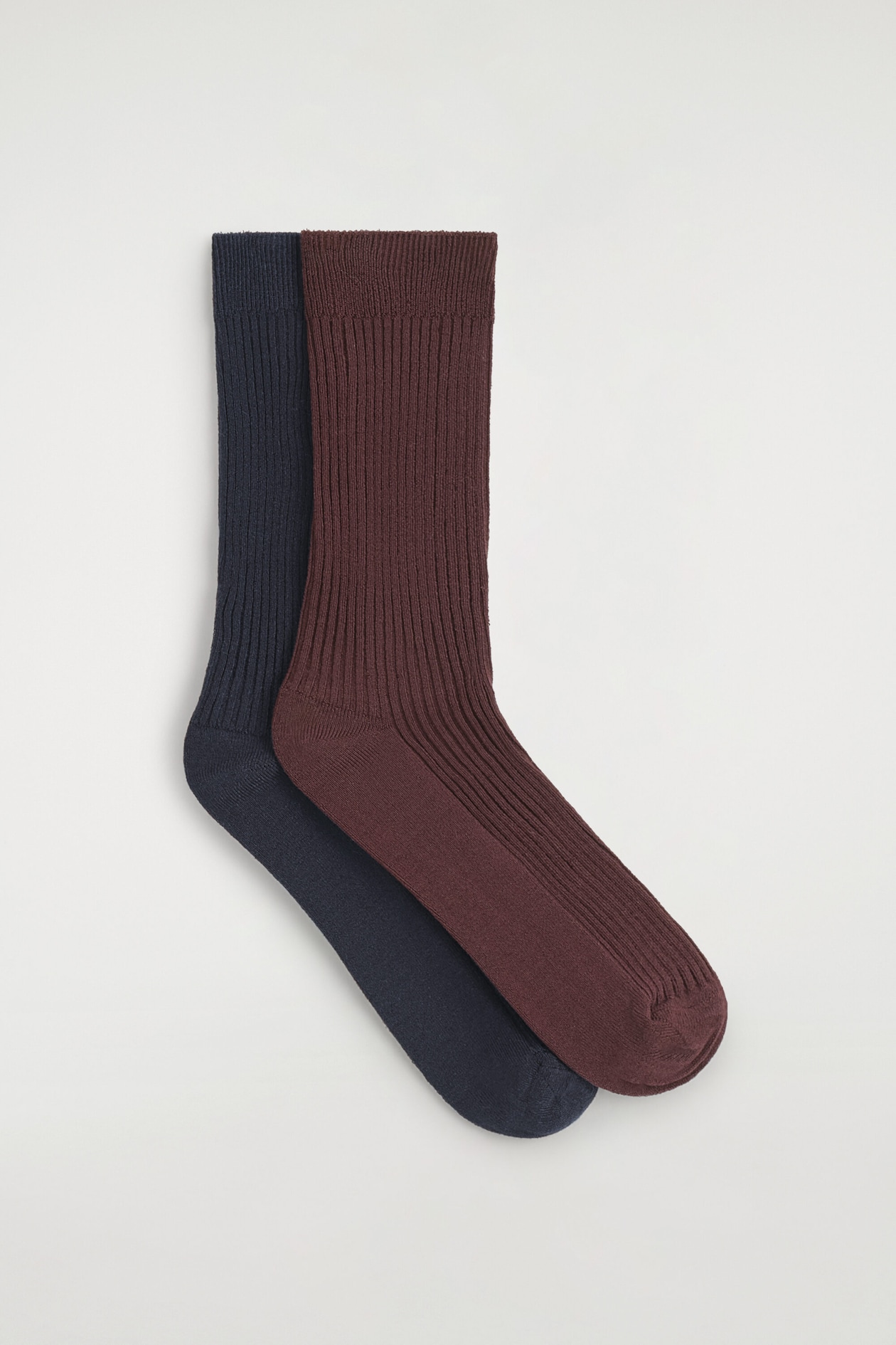 Un lot de 2 paires de chaussettes côtelées présente deux chaussettes posées à plat en vue de profil, avec une chaussette bordeaux foncé superposée à une chaussette bleu marine. Les deux chaussettes présentent une texture côtelée verticale tricotée le long de la tige et du dessus du pied, avec des pointes et des talons en maille lisse.