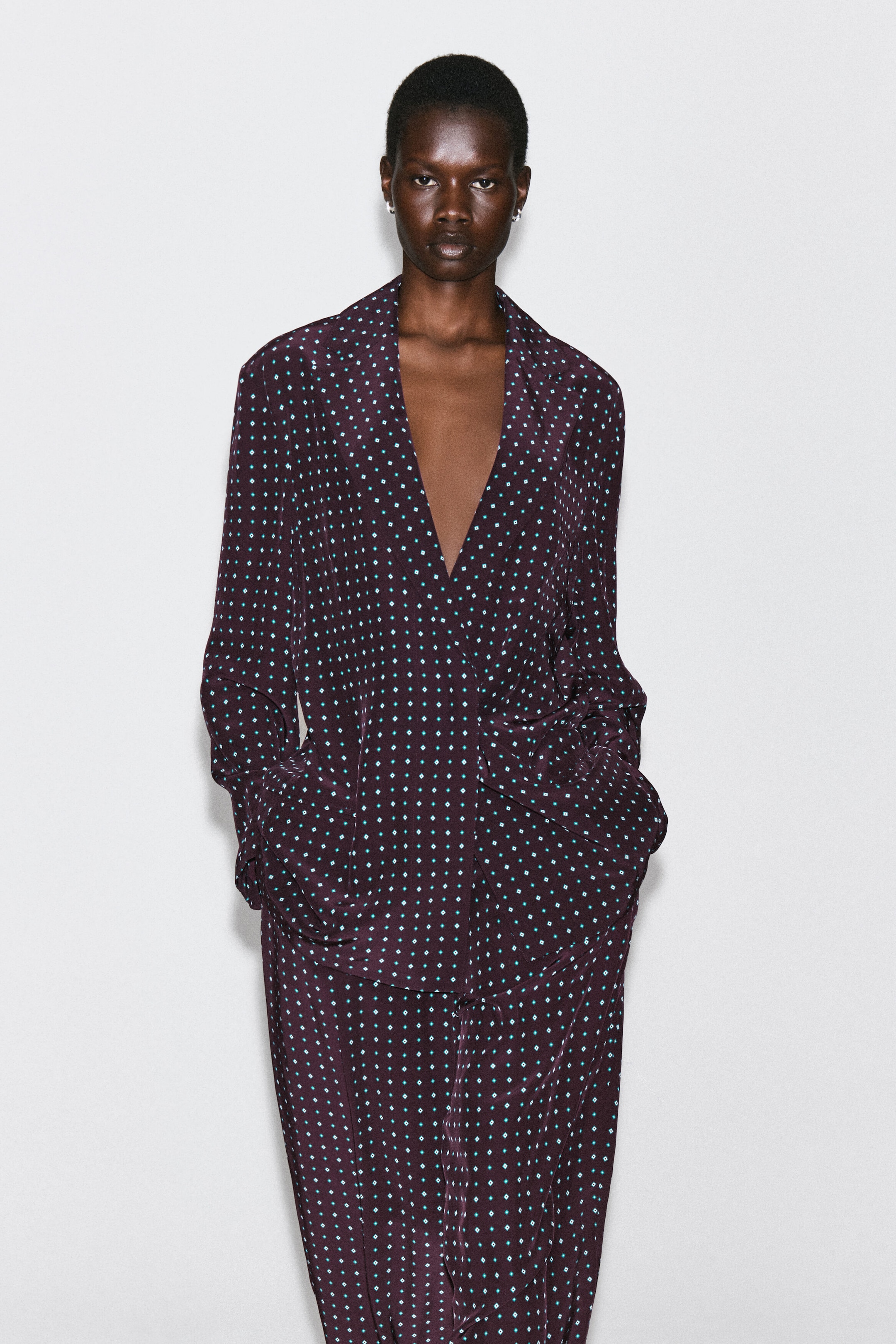 The diamond-print double-breasted blazer is presented in a relaxed fit from the front, showcasing dark plum fabric adorned with a repeating pattern of small teal and white diamonds. It features notch lapels and a deep V-neckline, and is paired with matching patterned trousers. The diamond-print double-breasted blazer is presented in a relaxed fit from the front, showcasing dark plum fabric adorned with a repeating pattern of small teal and white diamonds. It features notch lapels and a deep V-neckline, and is paired with matching patterned trousers.