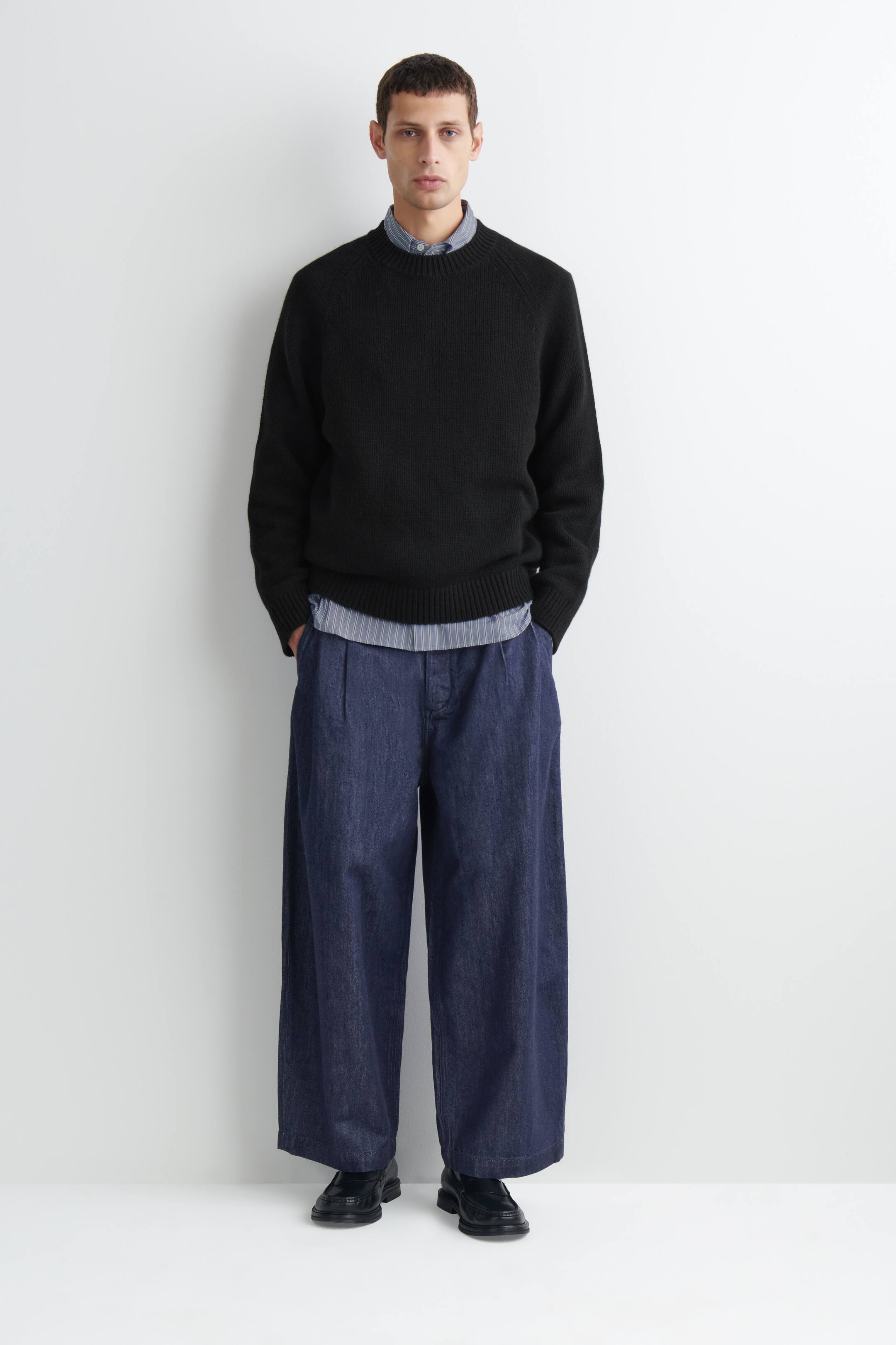 Agrandir l'image: Le pantalon barrel-leg en denim plissé à coupe décontractée, délavage bleu foncé, est présenté de face, avec une taille haute et des plis sur le devant, ainsi qu’une silhouette large aux jambes courbes. Il tombe amplement jusqu’aux chevilles, mettant en valeur son design volumineux et structuré.