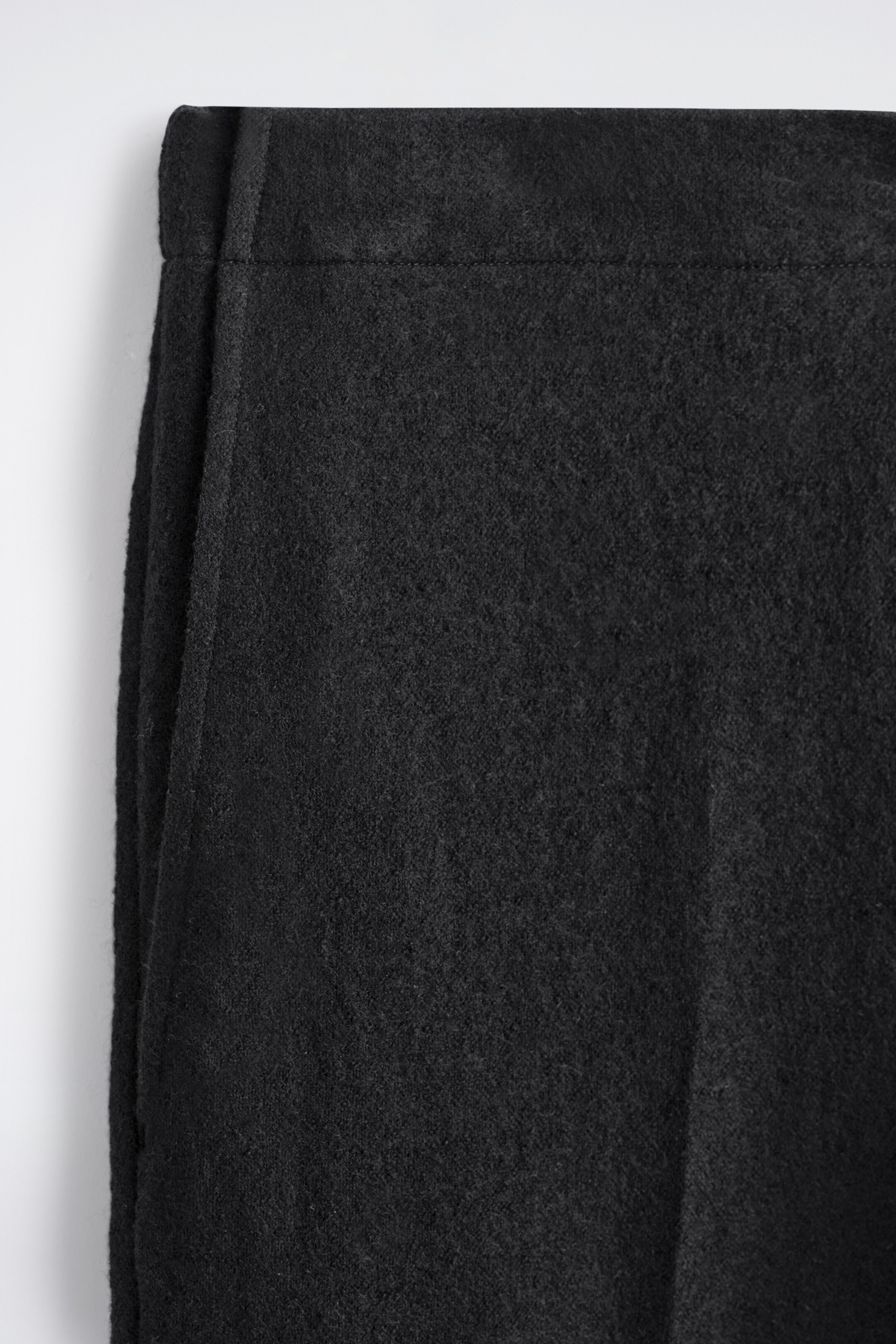 Agrandir l'image: Des pantalons en laine bouillie élastiquée sont présentés, en se concentrant sur la partie supérieure du vêtement. La texture dense et feutrée de la laine bouillie noire est visible, et un canal pour la ceinture élastiquée est formé par une couture horizontale sous le bord supérieur.