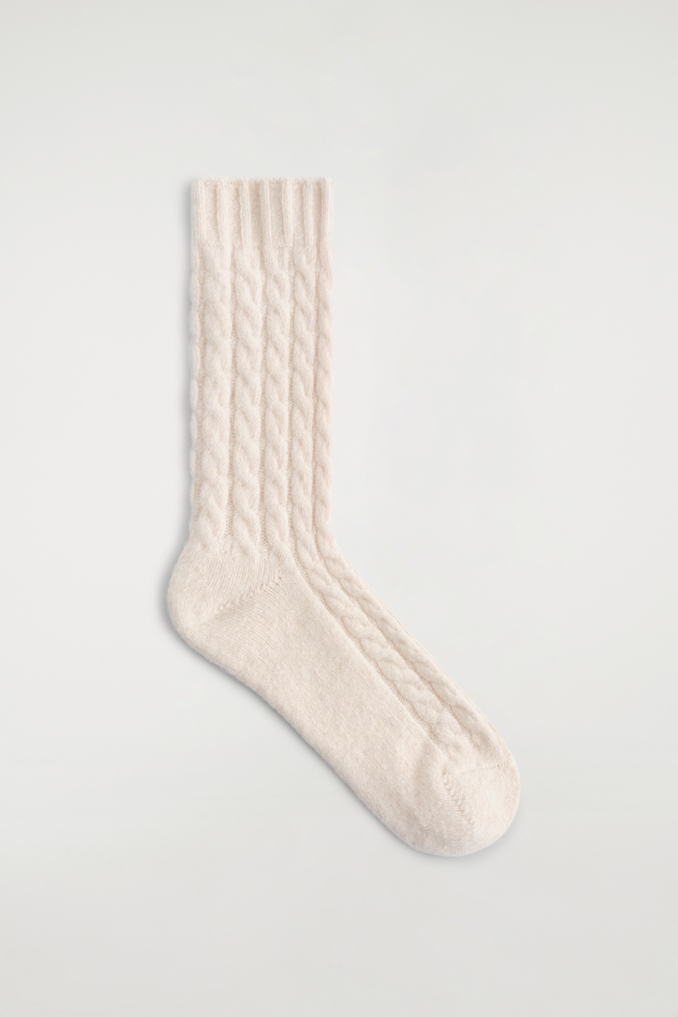 Ver imagen más grande: Un calcetín de punto trenzado de color crema presenta un puño acanalado en la parte superior, con el patrón trenzado extendiéndose por la pierna y un tejido liso en el pie.