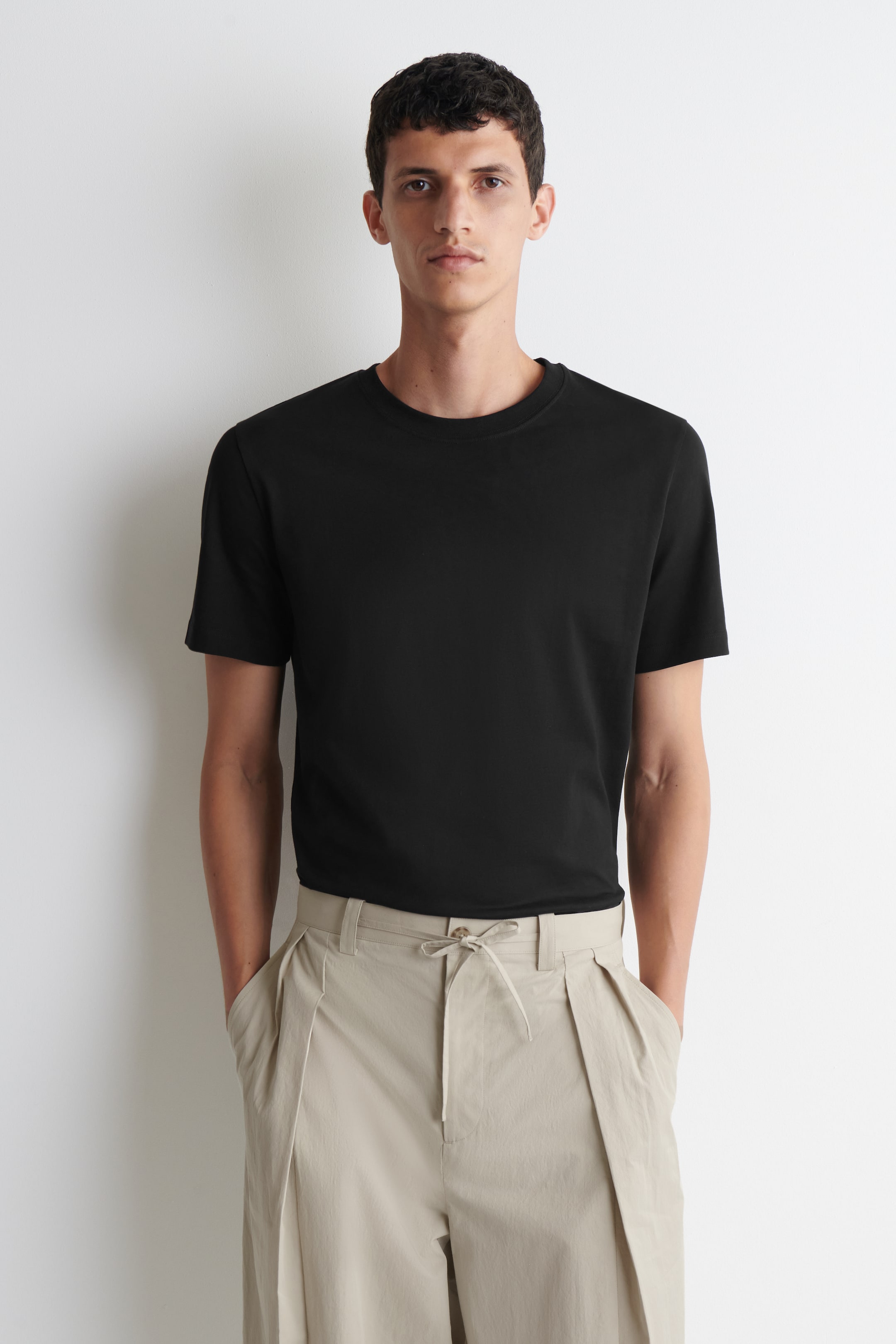 Grotere afbeelding bekijken: Een zwart t-shirt met ronde hals wordt van voren gedragen, waarbij de gladde, effen zwarte stof en korte mouwen worden getoond. Het zit comfortabel om de romp.