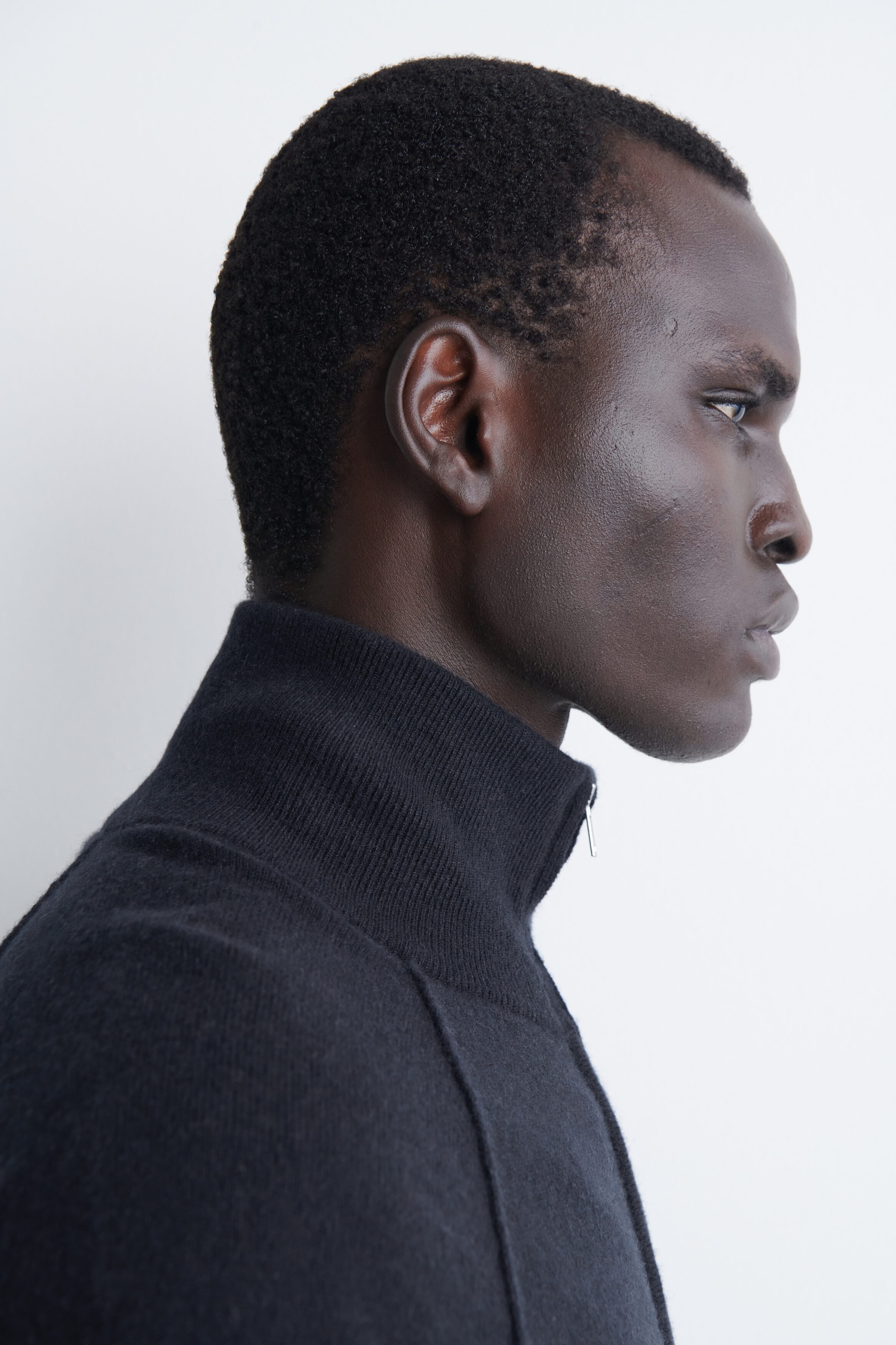 A dark cashmere funnel-neck zip-up cardigan is shown in right-facing profile, highlighting its high ribbed collar and silver-tone zip pull. The fine-knit garment features a raised seam running down from the collar line, emphasising its structured design. A dark cashmere funnel-neck zip-up cardigan is shown in right-facing profile, highlighting its high ribbed collar and silver-tone zip pull. The fine-knit garment features a raised seam running down from the collar line, emphasising its structured design.