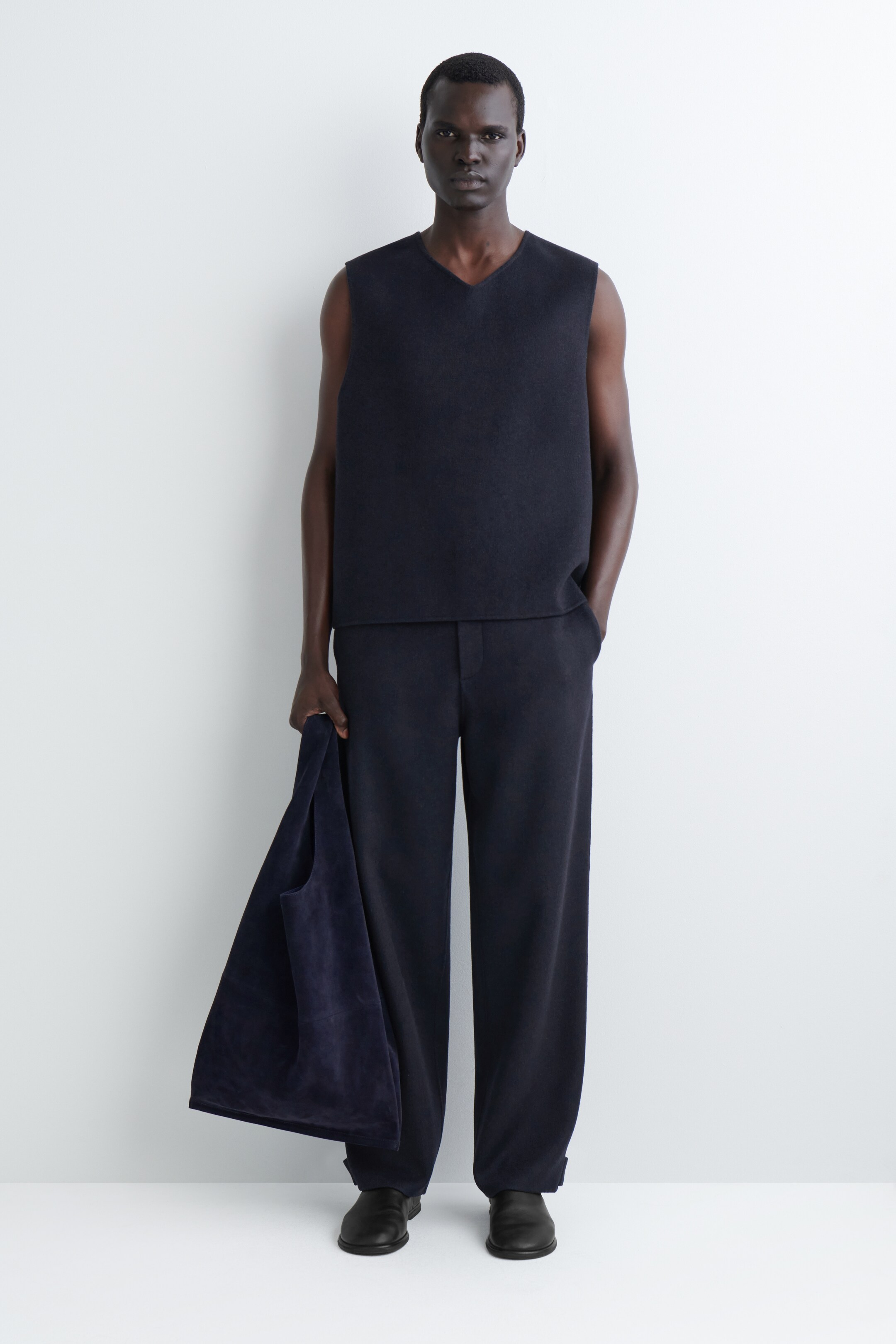 Agrandir l'image: Un ensemble bleu marine foncé, composé d'un haut sans manches à col en V et d'un pantalon à jambes larges, est présenté face avant. Un sac fourre-tout en tissu souple de couleur bleu marine foncé est tenu dans une main.