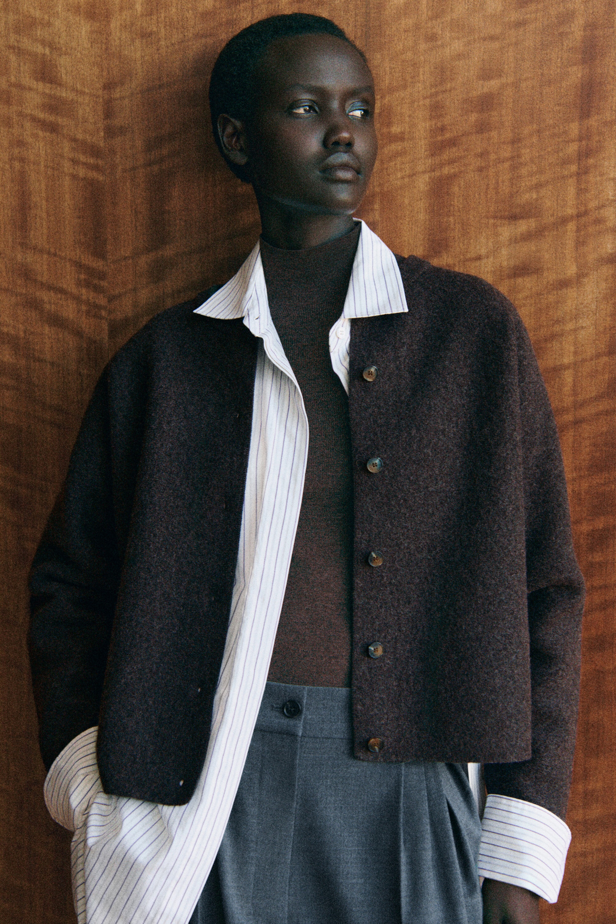 Eine dunkelbraune Cardigan aus gewalkter Wolle ist von vorn zu sehen und zeichnet sich durch eine entspannte, weich gerundete Silhouette sowie eine Knopfleiste vorn aus. Sie wird im Layering über einem gestreiften Hemd mit Kragen und einem braunen Oberteil mit hohem Halsausschnitt gestylt, wodurch ihre verkürzte Länge und die lässige Passform betont werden. Eine dunkelbraune Cardigan aus gewalkter Wolle ist von vorn zu sehen und zeichnet sich durch eine entspannte, weich gerundete Silhouette sowie eine Knopfleiste vorn aus. Sie wird im Layering über einem gestreiften Hemd mit Kragen und einem braunen Oberteil mit hohem Halsausschnitt gestylt, wodurch ihre verkürzte Länge und die lässige Passform betont werden.