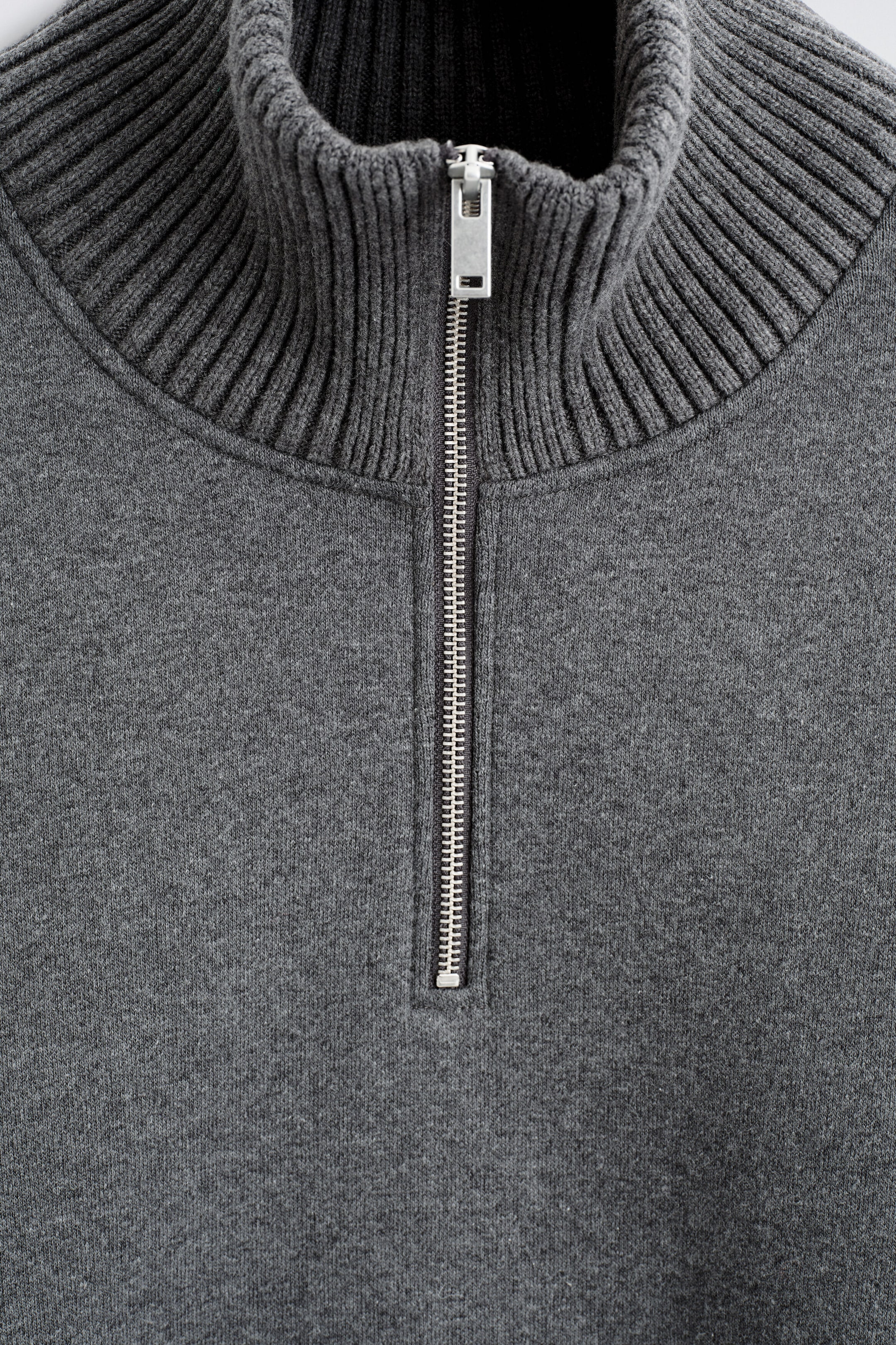 This close-up front view of the cotton-wool jersey zip-up jumper shows a ribbed high collar and a silver-tone metal half-zip fastening with a rectangular pull tab. The jumper features a dark grey jersey-knit body with a clean, structured design. This close-up front view of the cotton-wool jersey zip-up jumper shows a ribbed high collar and a silver-tone metal half-zip fastening with a rectangular pull tab. The jumper features a dark grey jersey-knit body with a clean, structured design.
