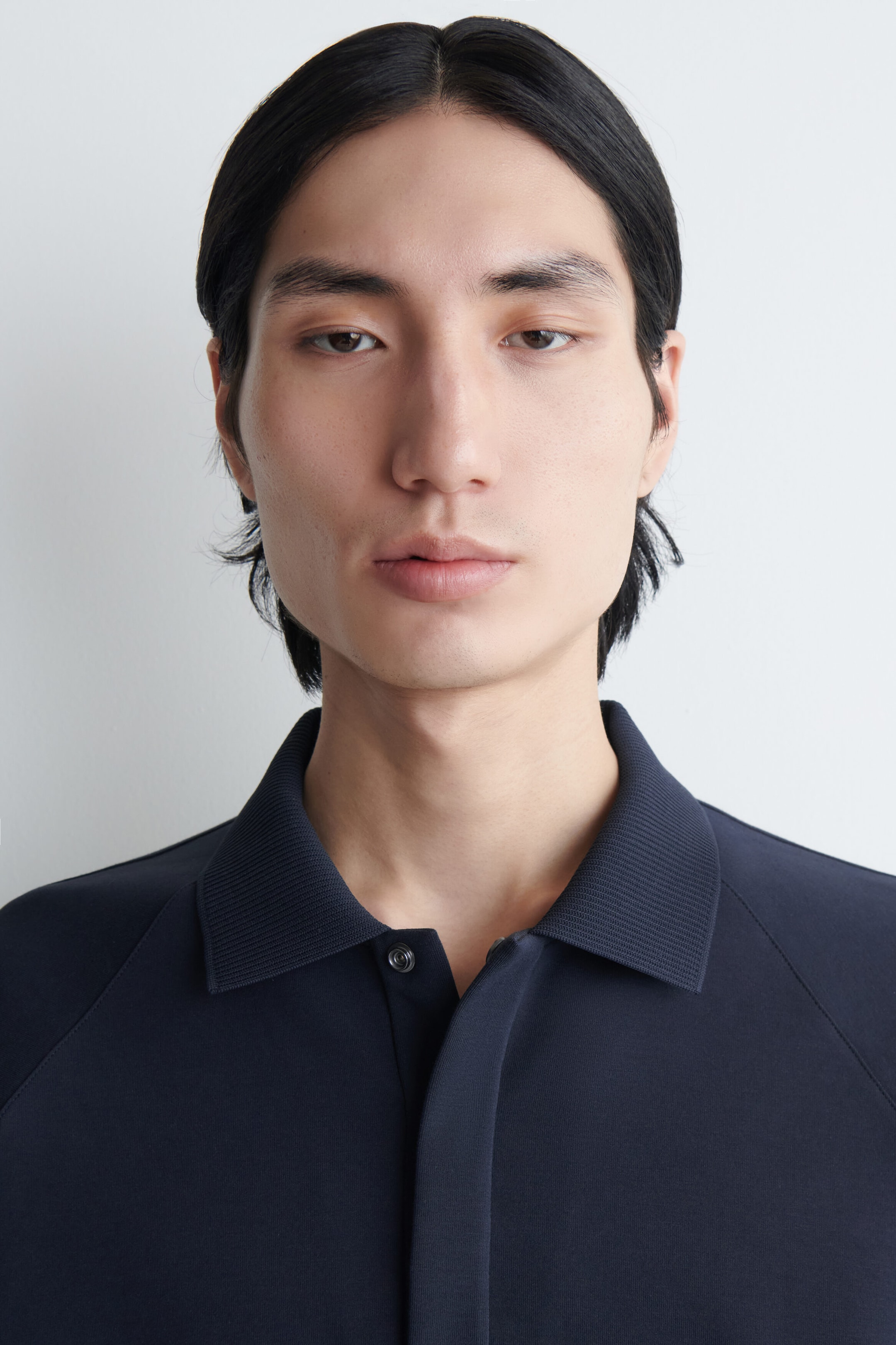 The model is wearing a navy blue scuba jersey polo shirt featuring a structured design with raglan sleeves. The shirt is styled with a fine-ribbed collar and a partially concealed button placket. The model is wearing a navy blue scuba jersey polo shirt featuring a structured design with raglan sleeves. The shirt is styled with a fine-ribbed collar and a partially concealed button placket.