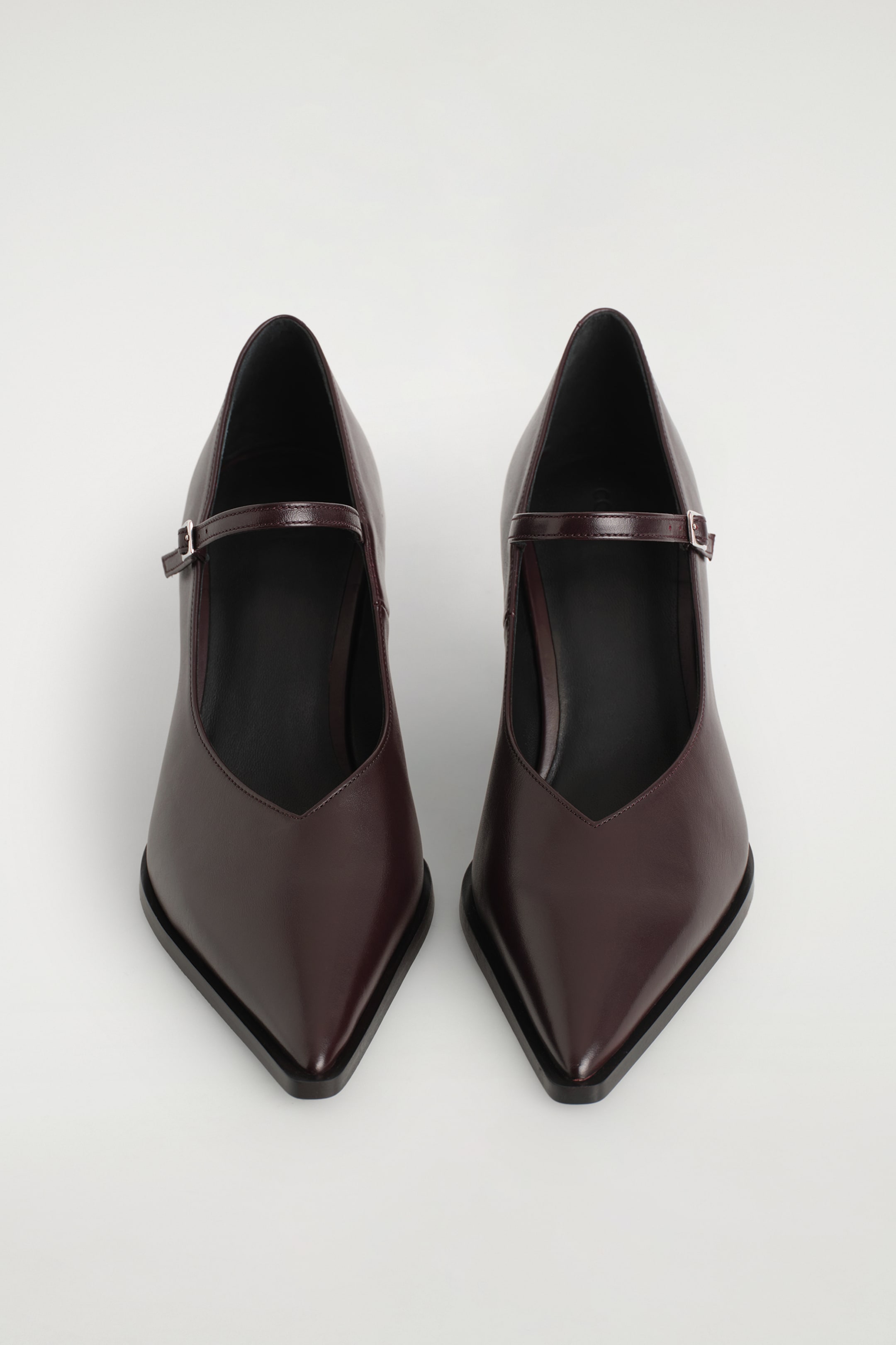 Agrandir l'image: Une paire de chaussures Mary Jane à talons en cuir bordeaux foncé est exposée, chacune avec un bout pointu, un décolleté en V et une fine bride avec une boucle argentée qui s'étend sur le cou-de-pied.