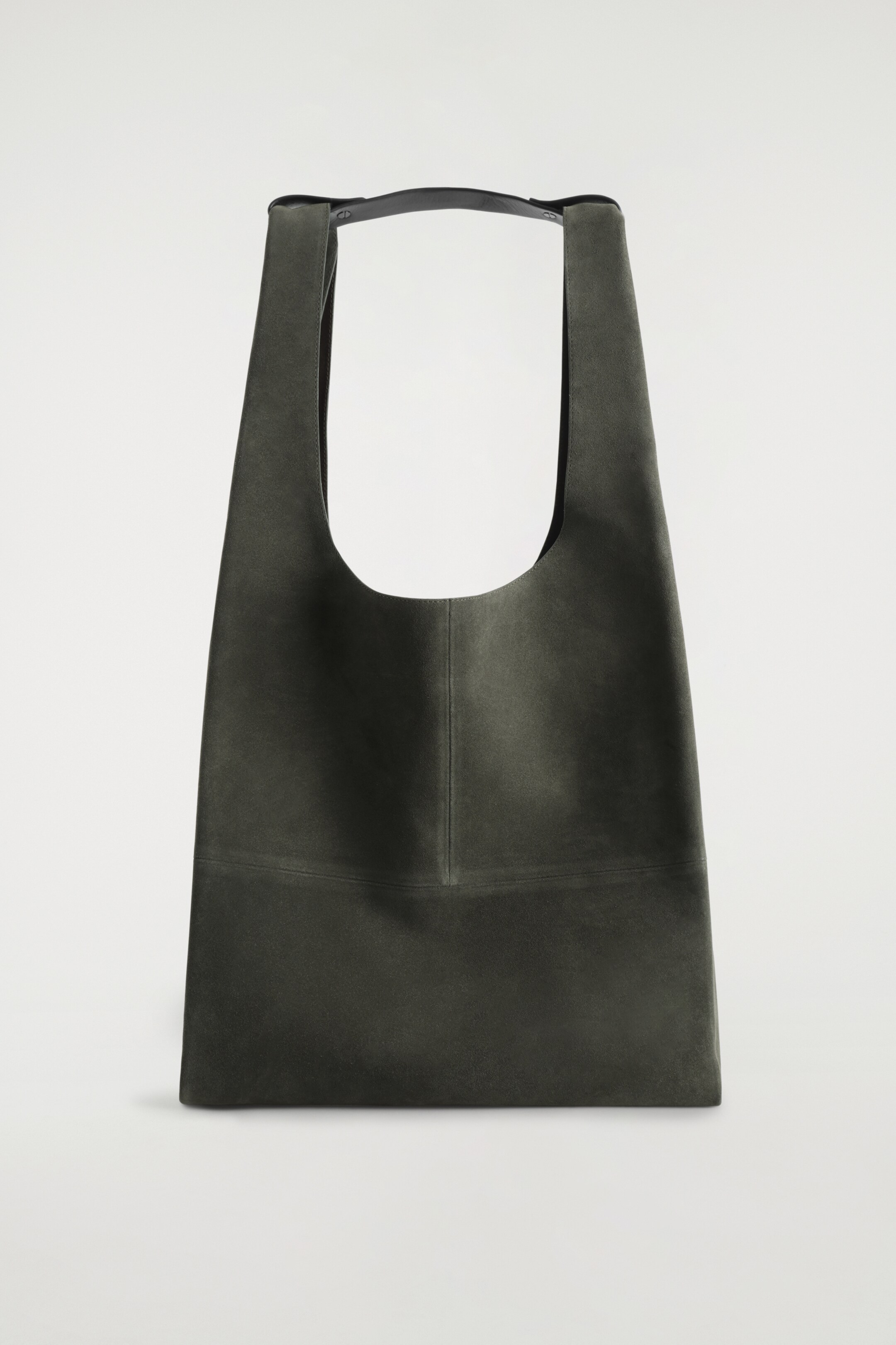 Agrandir l'image: Un sac fourre-tout en daim vert olive foncé présente son devant, avec une large ouverture en forme de U en haut, une couture verticale au centre et une couture horizontale sur le bas de son devant. Deux anses d'épaule en cuir noir émergent du haut, fixées par une patte en cuir horizontale.