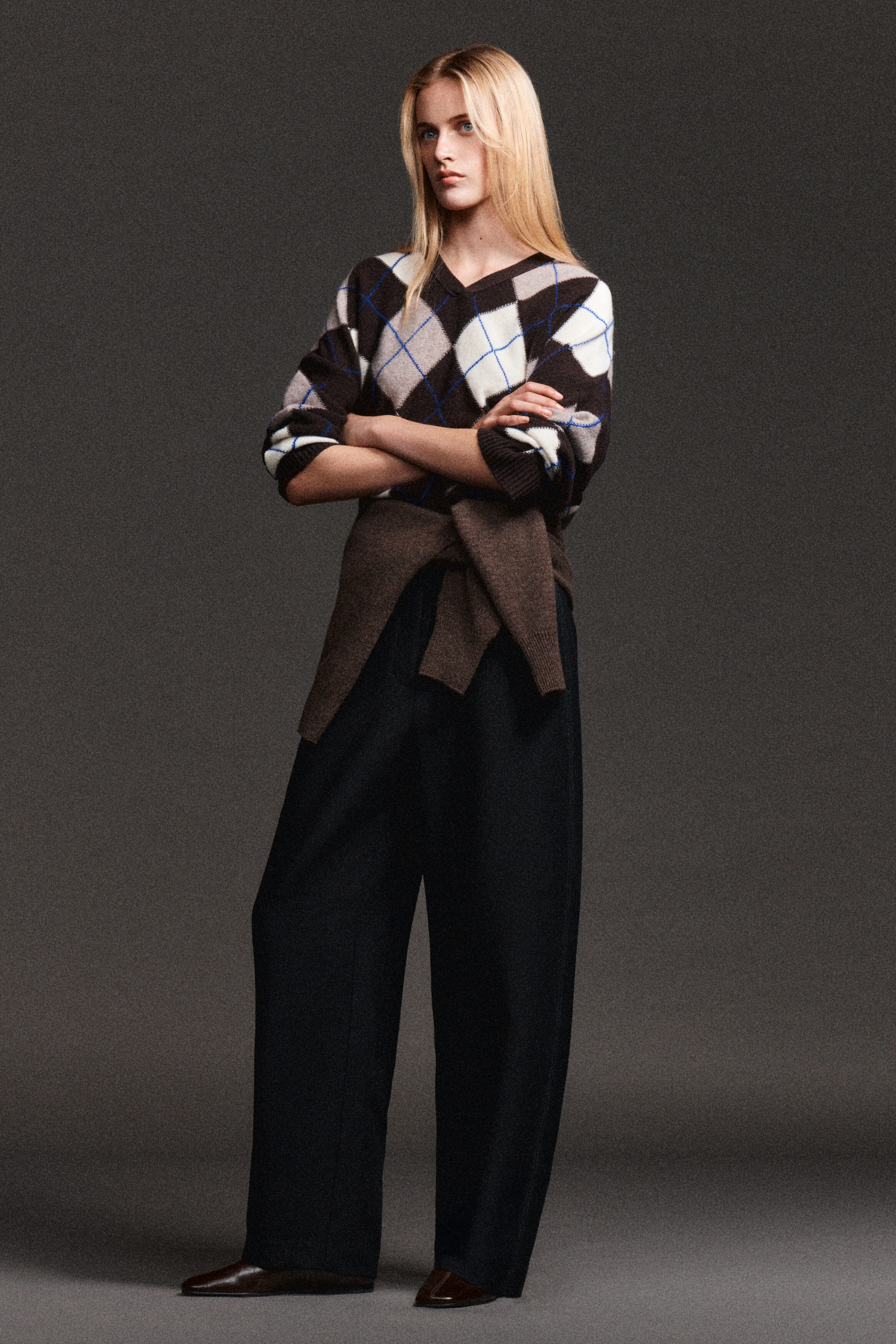 Topstitched barrel-leg trousers are shown from the front, highlighting their dark fabric and structured, curved barrel-leg silhouette. The trousers fall to a full-length hem, with a brown knit jumper tied around the waist. Topstitched barrel-leg trousers are shown from the front, highlighting their dark fabric and structured, curved barrel-leg silhouette. The trousers fall to a full-length hem, with a brown knit jumper tied around the waist.