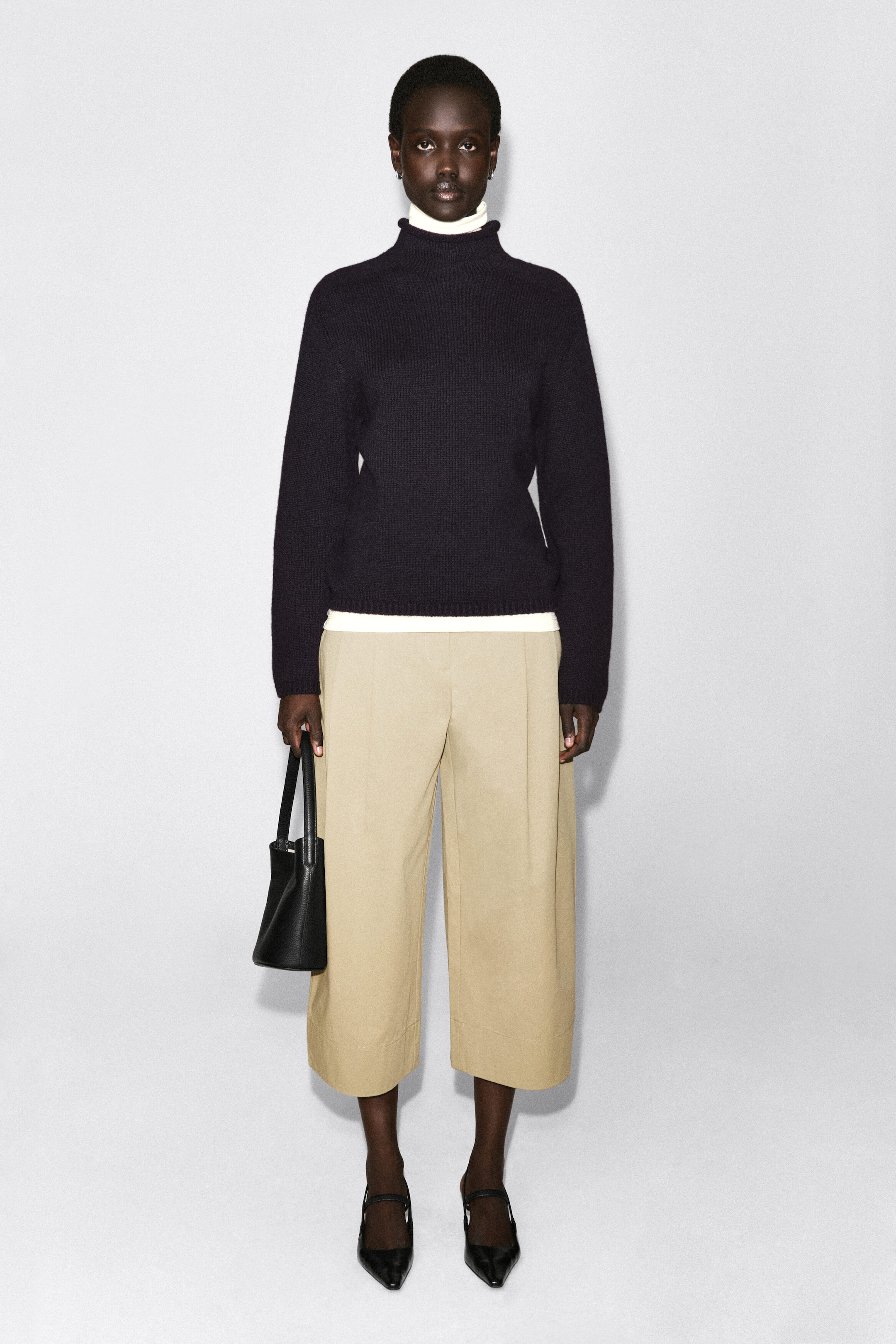 Cotton cropped barrel-leg pants in a beige hue are shown from the front, showcasing a structured, curved silhouette that tapers slightly at the cropped hem. The pants fall to mid-calf with visible front creases, while the waistband is partially covered by a layered sweater. Cotton cropped barrel-leg pants in a beige hue are shown from the front, showcasing a structured, curved silhouette that tapers slightly at the cropped hem. The pants fall to mid-calf with visible front creases, while the waistband is partially covered by a layered sweater.