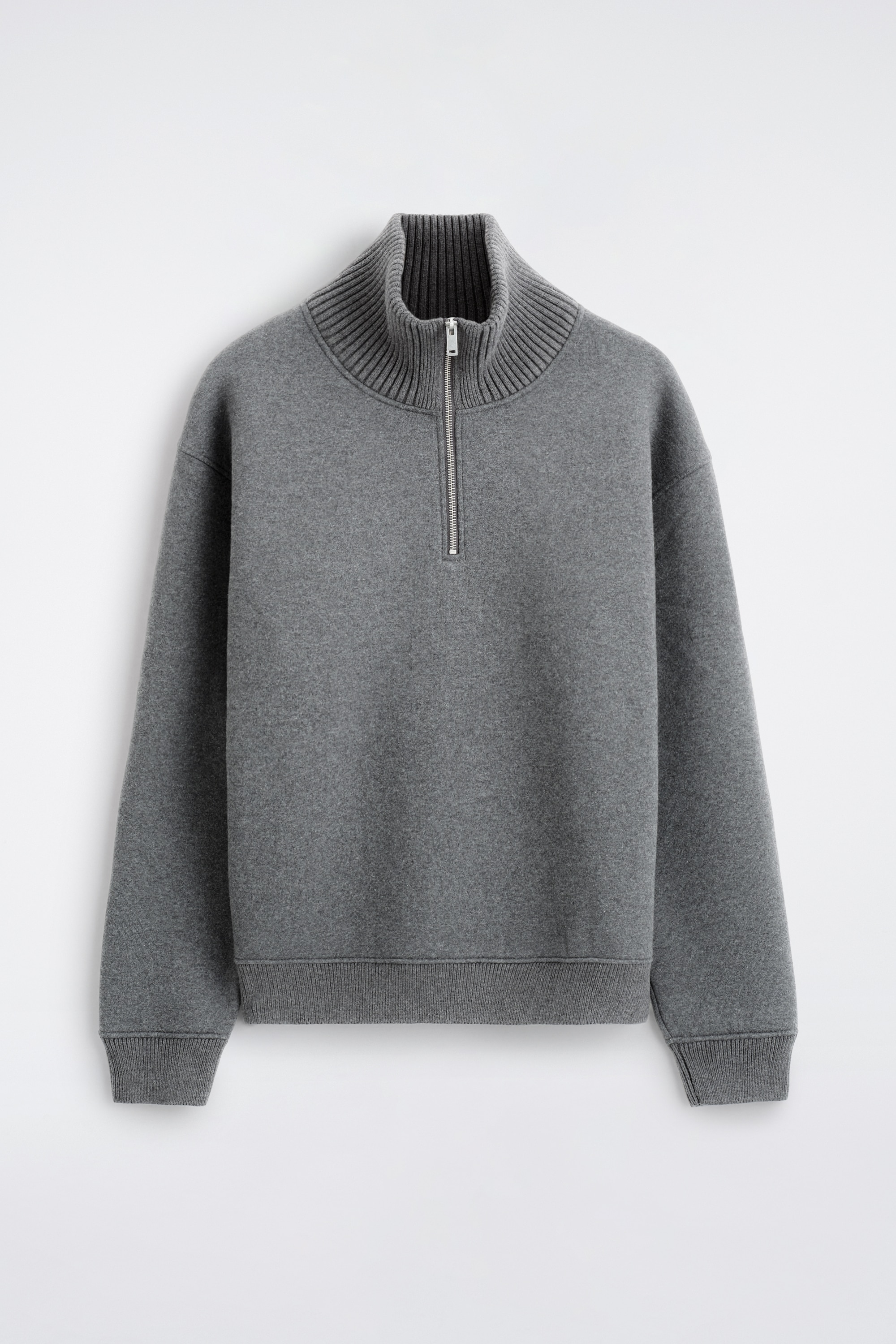 Le mannequin porte un pull zippÃ© en jersey gris en coton et laine, dotÃ© dâun col montant cÃ´telÃ© avec une fermeture demi-zip ton argentÃ©. Le pull est portÃ© avec un pantalon noir et prÃ©sente des poignets cÃ´telÃ©s ainsi quâun ourlet cÃ´telÃ©.