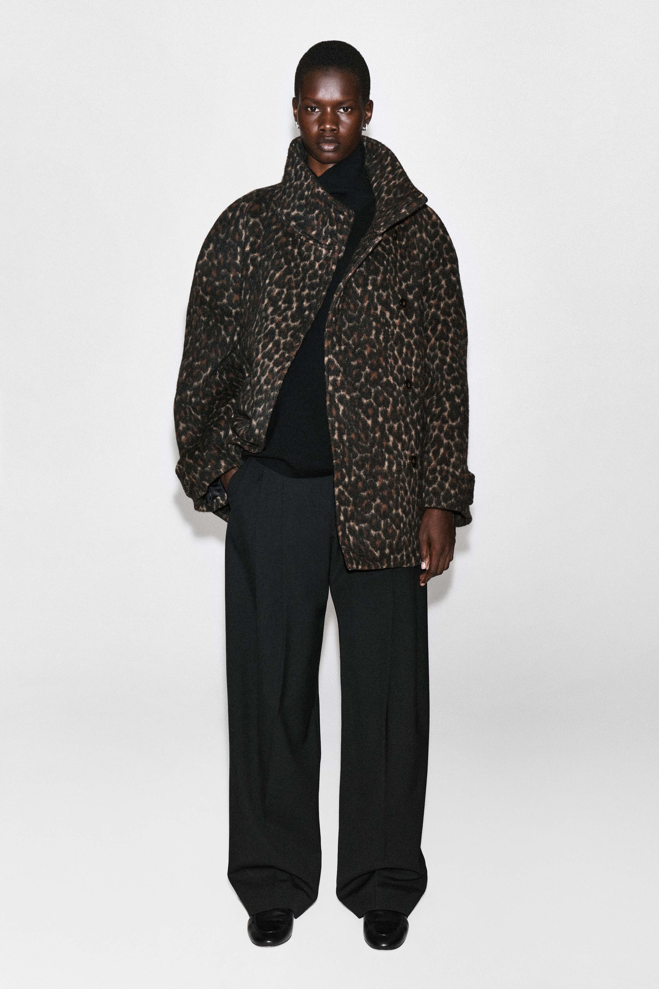 Ein Mantel aus Wollmischung mit Leopardenmuster und Stehkragen wird vom Model getragen, kombiniert mit einem schwarzen Oberteil mit hohem Kragen und schwarzen weiten Hosen. Ein Mantel aus Wollmischung mit Leopardenmuster und Stehkragen wird vom Model getragen, kombiniert mit einem schwarzen Oberteil mit hohem Kragen und schwarzen weiten Hosen.