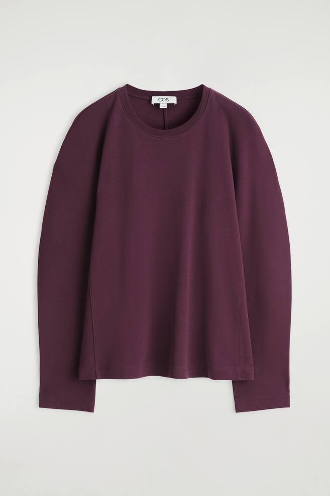 Ein dunkelrotes Langarmshirt wird von vorne gezeigt, mit einem gerippten Rundhalsausschnitt, entspannten, abgerundeten Ärmeln und dezenten Seitennähten, die eine leicht taillierte Silhouette definieren. - 1