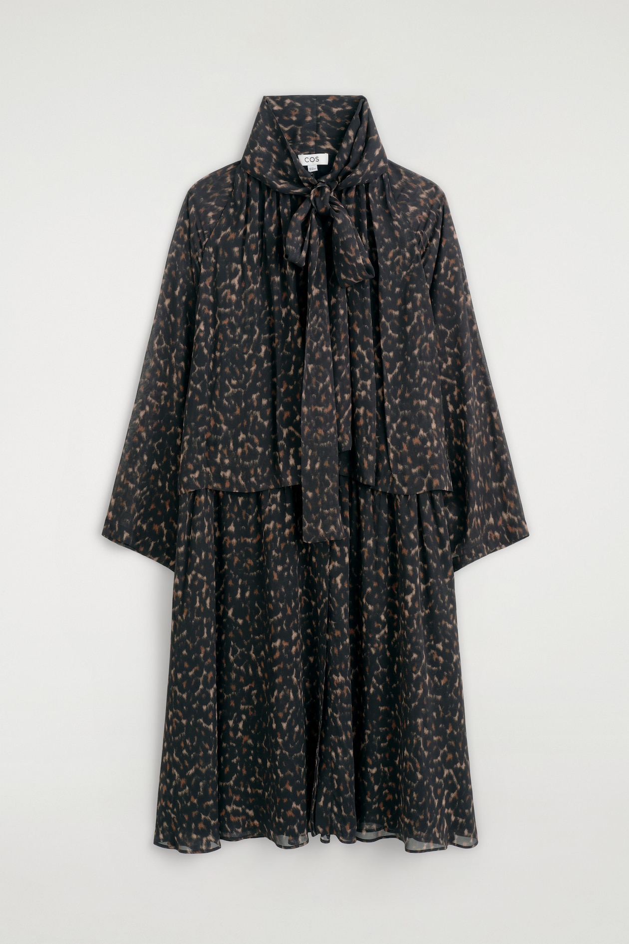 The leopard-print fluid dress with scarf detail is shown hanging in a front view, featuring a high collar with a self-tie scarf detail knotted at the neck. It has wide, long sleeves, a layered bodice design, and a relaxed, fluid silhouette with an all-over brown and black leopard pattern.
