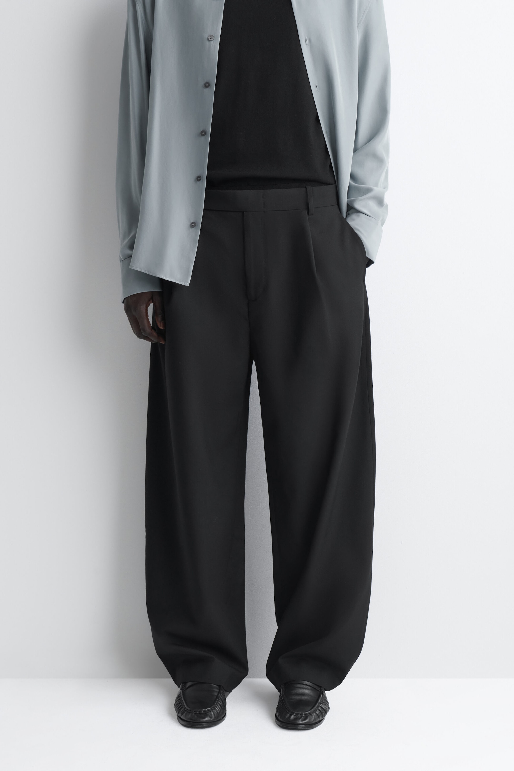 Die schwarzen Barrel-Leg-Hosen aus Wolle im Relaxed Fit zeichnen sich durch eine geschwungene, weit geschnittene Silhouette mit vorderen Faltendetails und einem strukturierten Bund aus. Die Hose fällt locker bis zum Saum und ist mit einem in den Bund gesteckten schwarzen Oberteil gestylt, um das Taillendesign hervorzuheben. Die schwarzen Barrel-Leg-Hosen aus Wolle im Relaxed Fit zeichnen sich durch eine geschwungene, weit geschnittene Silhouette mit vorderen Faltendetails und einem strukturierten Bund aus. Die Hose fällt locker bis zum Saum und ist mit einem in den Bund gesteckten schwarzen Oberteil gestylt, um das Taillendesign hervorzuheben.