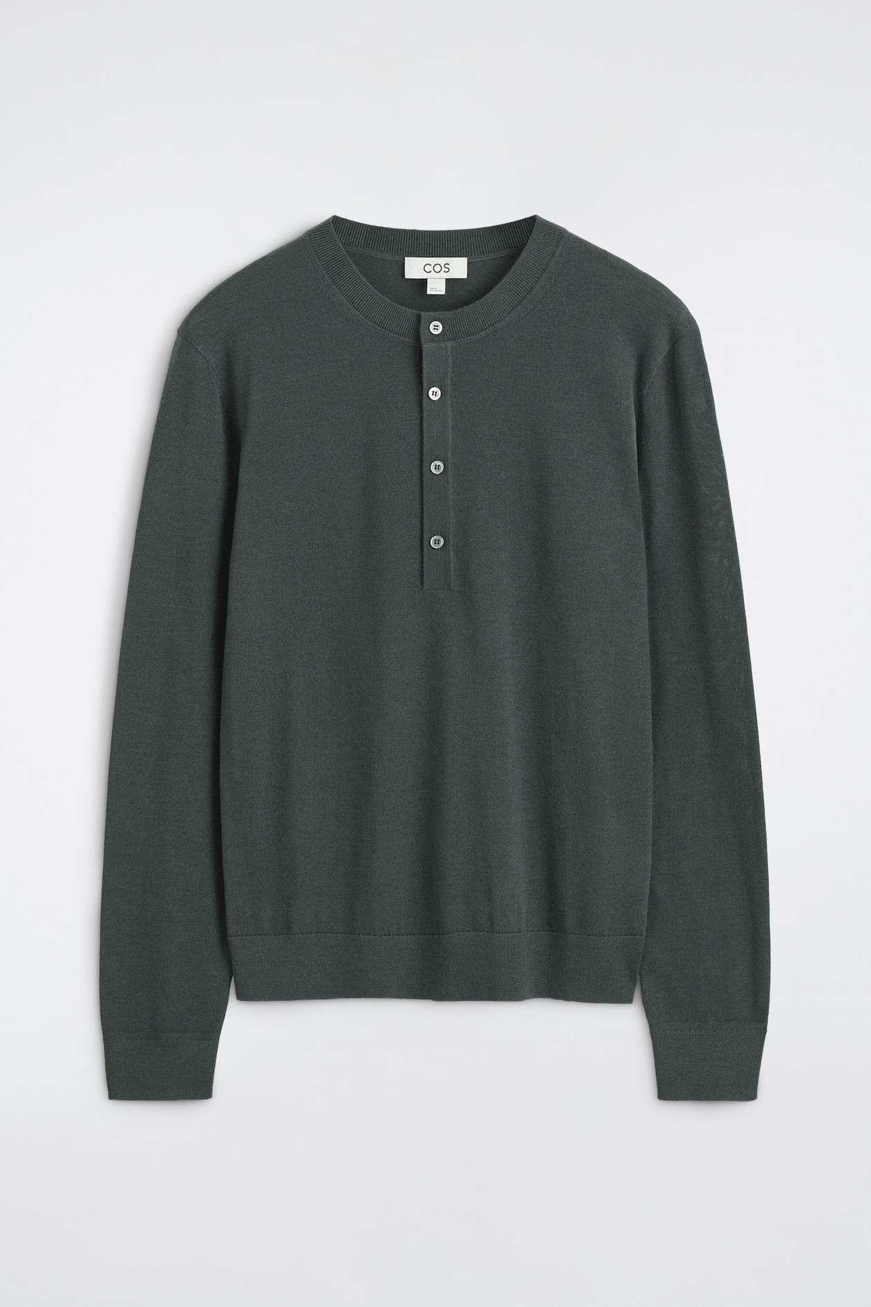 A slim merino wool Henley top in dark green is shown from the front, featuring a ribbed crew neck, a four-button placket, and long sleeves. The top is finished with ribbed cuffs and a ribbed hem.