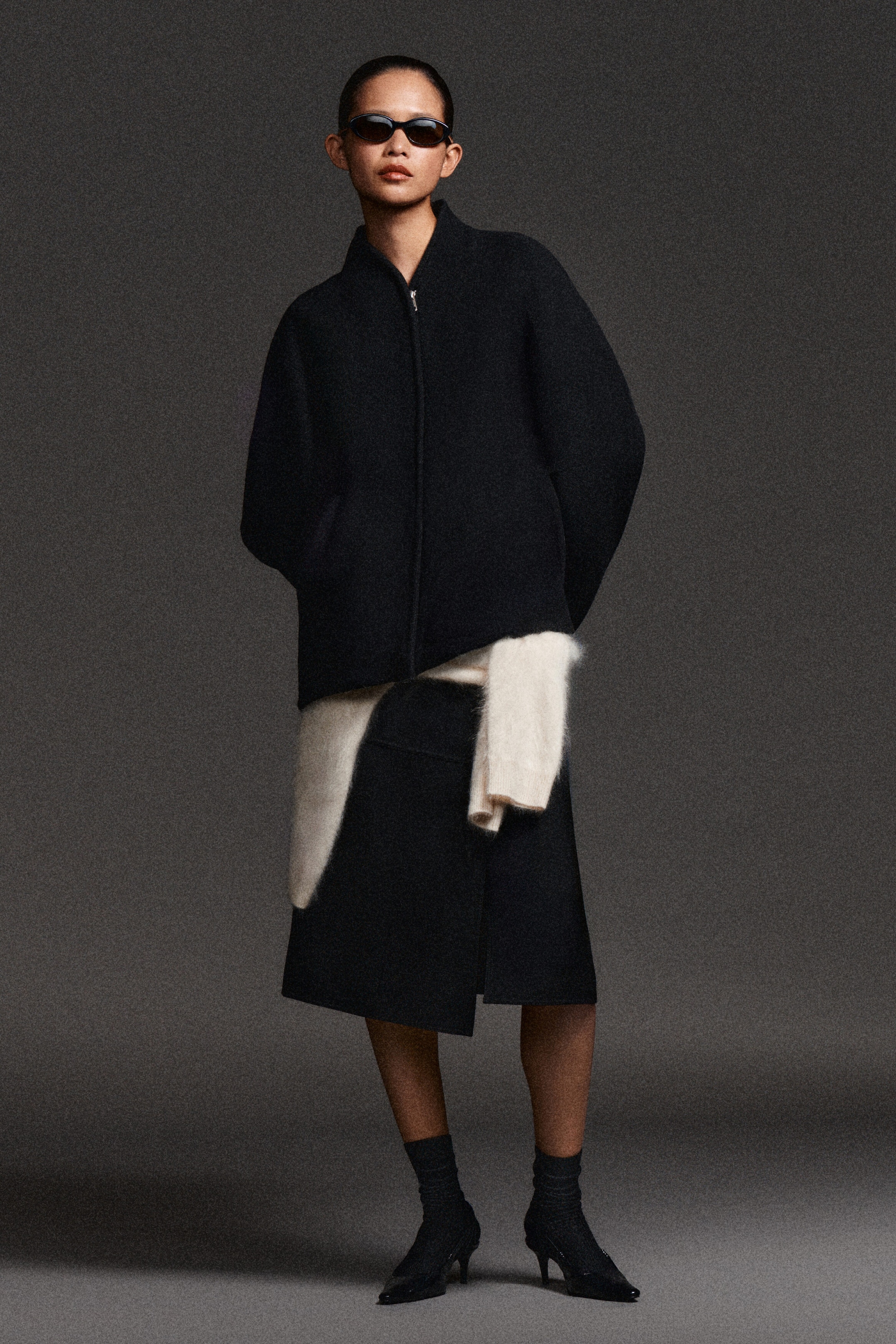 The black sculpted wool-blend zip-up jacket is shown from a front-facing angle, with a structured, rounded silhouette, featuring a high stand collar and a central zip fastening. The jacket drapes over the torso with clean lines, highlighting its thick, textured fabric and relaxed sleeves. The black sculpted wool-blend zip-up jacket is shown from a front-facing angle, with a structured, rounded silhouette, featuring a high stand collar and a central zip fastening. The jacket drapes over the torso with clean lines, highlighting its thick, textured fabric and relaxed sleeves.