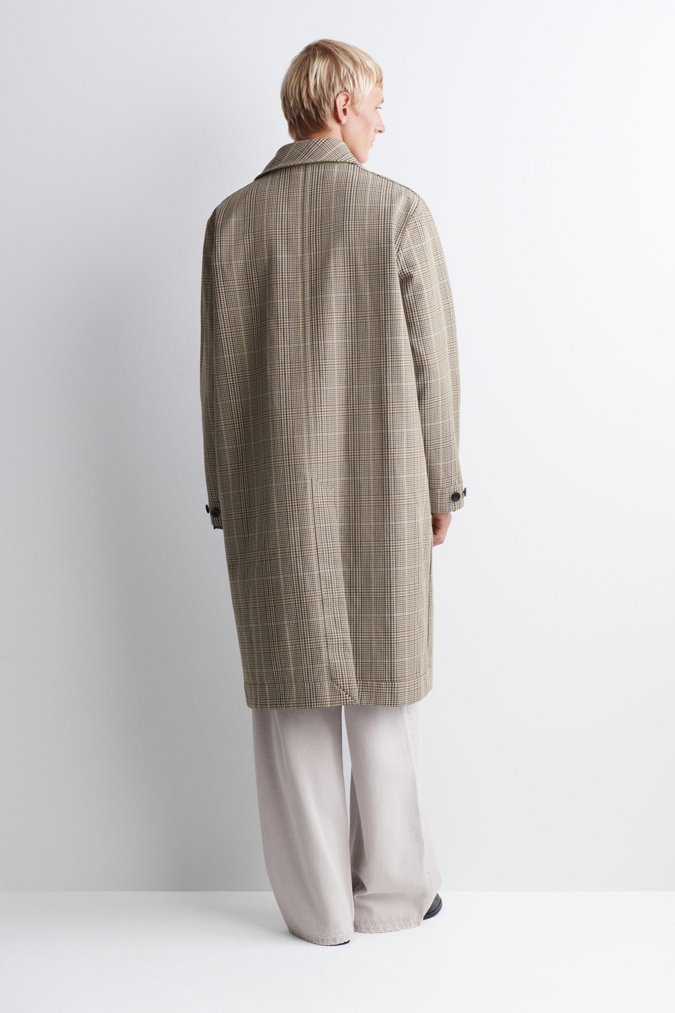 Le car coat réversible à carreaux est présenté de dos, avec un motif à carreaux beige et brun, un col classique et une seule fente d’aisance au dos à l’ourlet. Ce manteau coupe décontractée, longueur genou, est porté avec un pantalon large de couleur claire, mettant en valeur sa silhouette droite et ses pattes boutonnées aux poignets. Le car coat réversible à carreaux est présenté de dos, avec un motif à carreaux beige et brun, un col classique et une seule fente d’aisance au dos à l’ourlet. Ce manteau coupe décontractée, longueur genou, est porté avec un pantalon large de couleur claire, mettant en valeur sa silhouette droite et ses pattes boutonnées aux poignets.