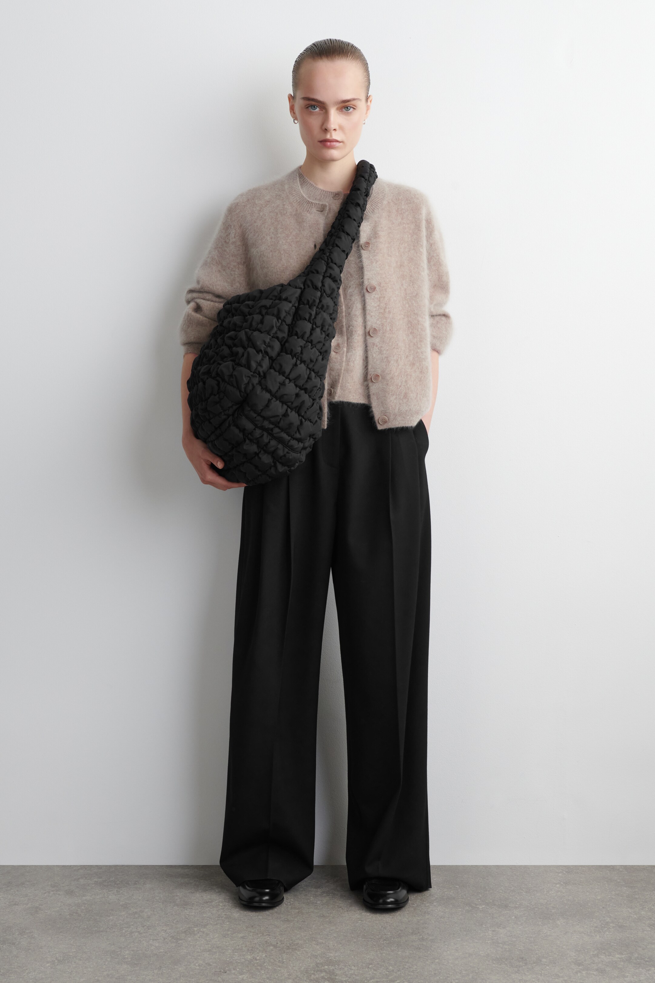 Visualizza immagine più grande: La borsa nera oversize trapuntata è indossata attraverso il corpo, con la sua ampia tracolla imbottita che poggia sulla spalla destra. Il davanti della borsa mostra una texture trapuntata particolare e morbida, apparendo soffice e senza struttura.