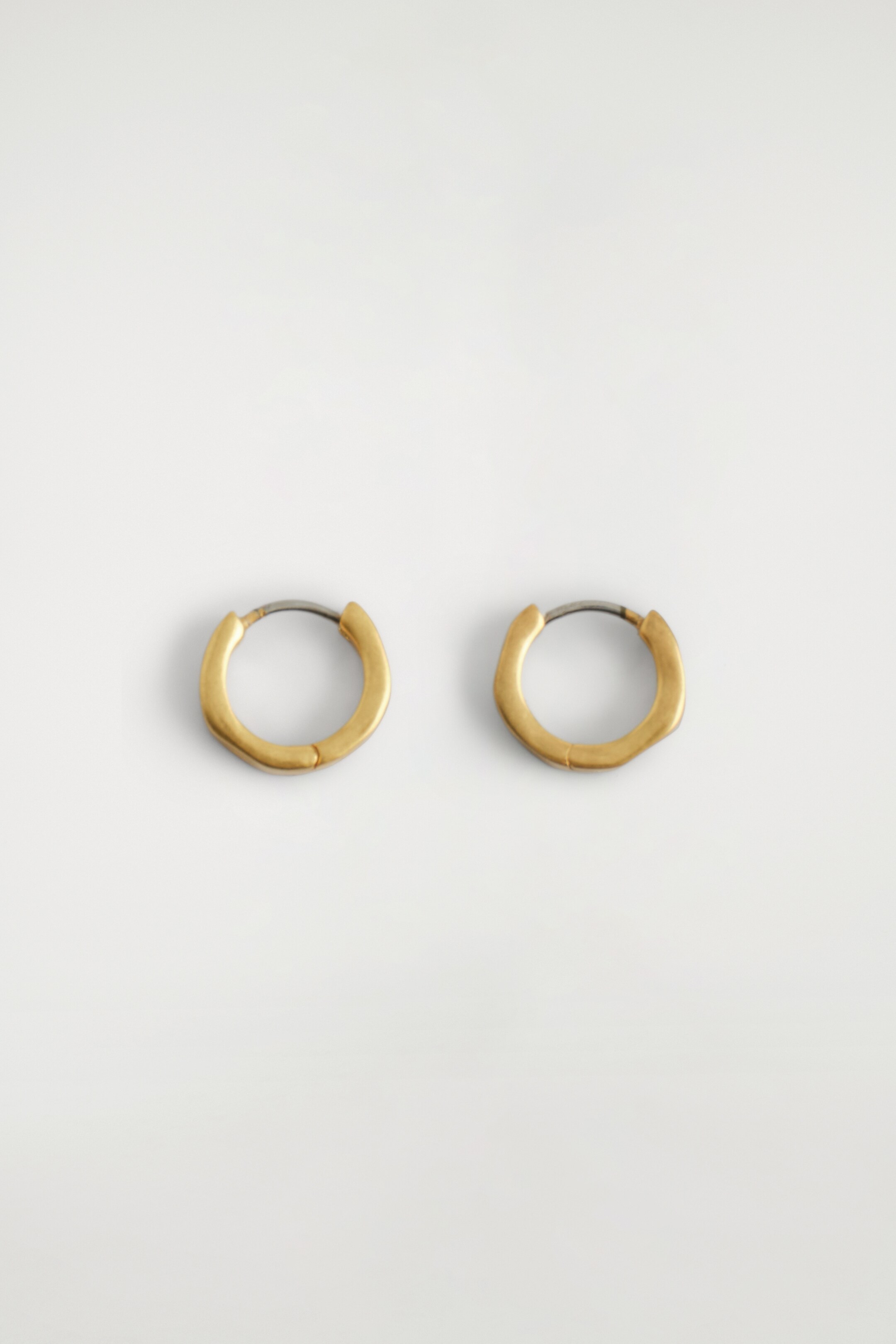 Agrandir l'image: Deux boucles d'oreilles mini créoles martelées de ton doré sont présentées côte à côte. Chaque boucle d'oreille présente une surface texturée avec des indentations subtiles, et un fermoir en métal plus foncé est visible à son sommet.