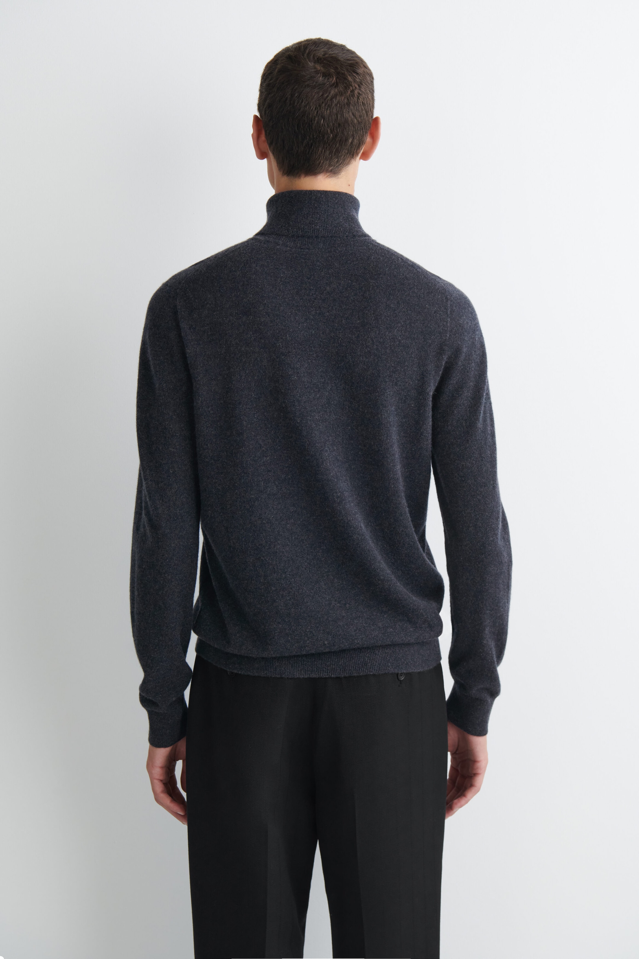 Un pull col roulé en pur cachemire gris foncé est présenté de dos, mettant en valeur sa coupe regular, son col roulé montant, ses poignets côtelés et son ourlet côtelé. Le pull est porté avec un pantalon noir. Un pull col roulé en pur cachemire gris foncé est présenté de dos, mettant en valeur sa coupe regular, son col roulé montant, ses poignets côtelés et son ourlet côtelé. Le pull est porté avec un pantalon noir.