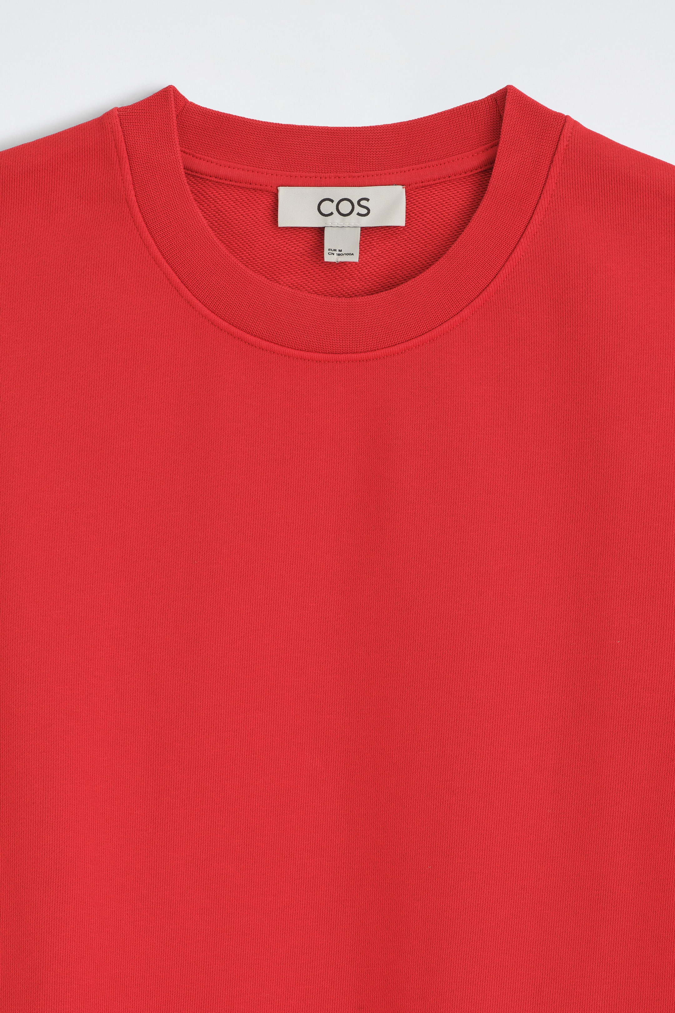 A close-up front view of a red sweatshirt showcasing its ribbed crew neck and inner brand label. A close-up front view of a red sweatshirt showcasing its ribbed crew neck and inner brand label.