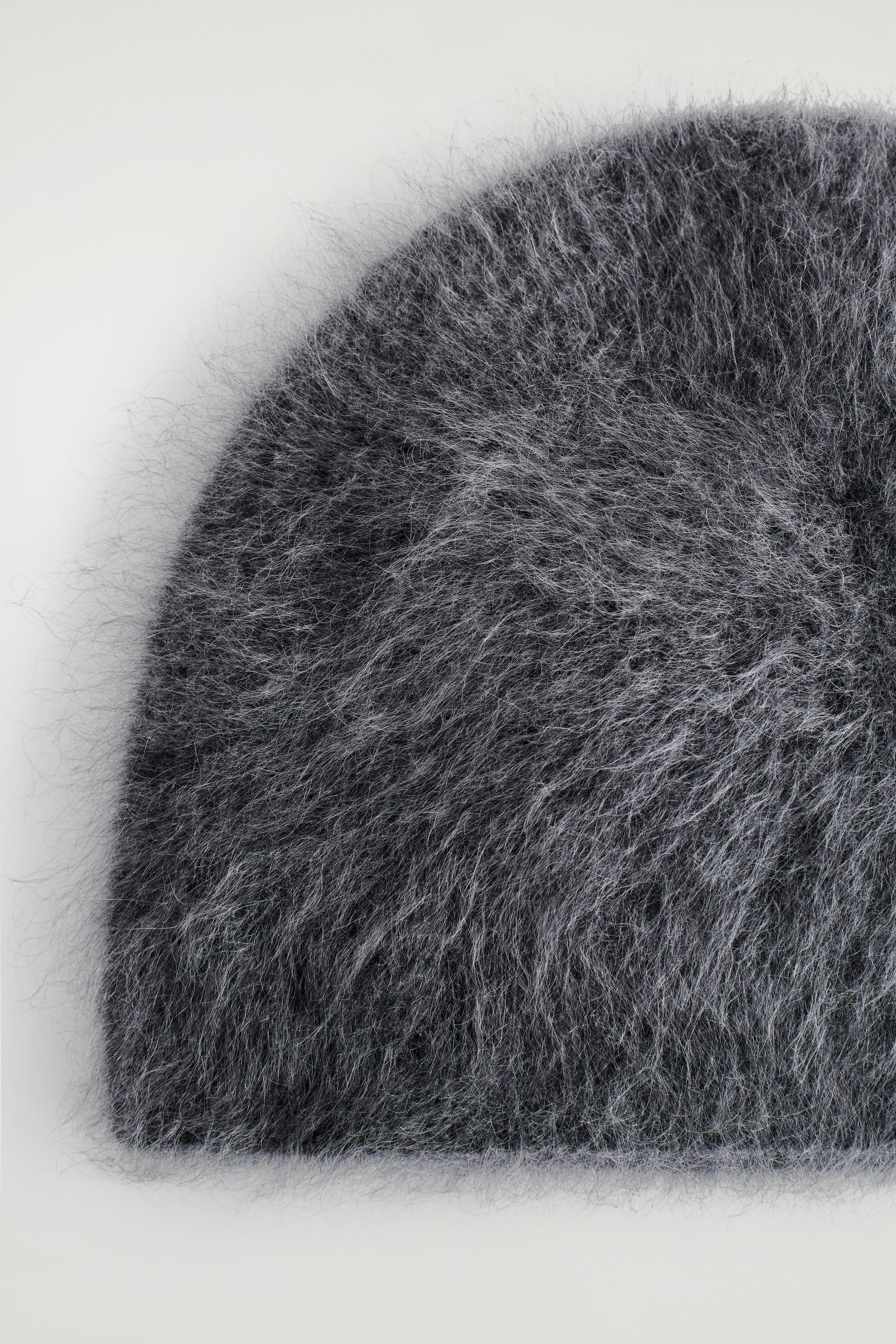 Agrandir l'image: Un bonnet en charbon est montré en gros plan, sa surface apparaissant brossée et douce. Des fibres individuelles s'étendent visiblement du tissu, créant une texture duveteuse.