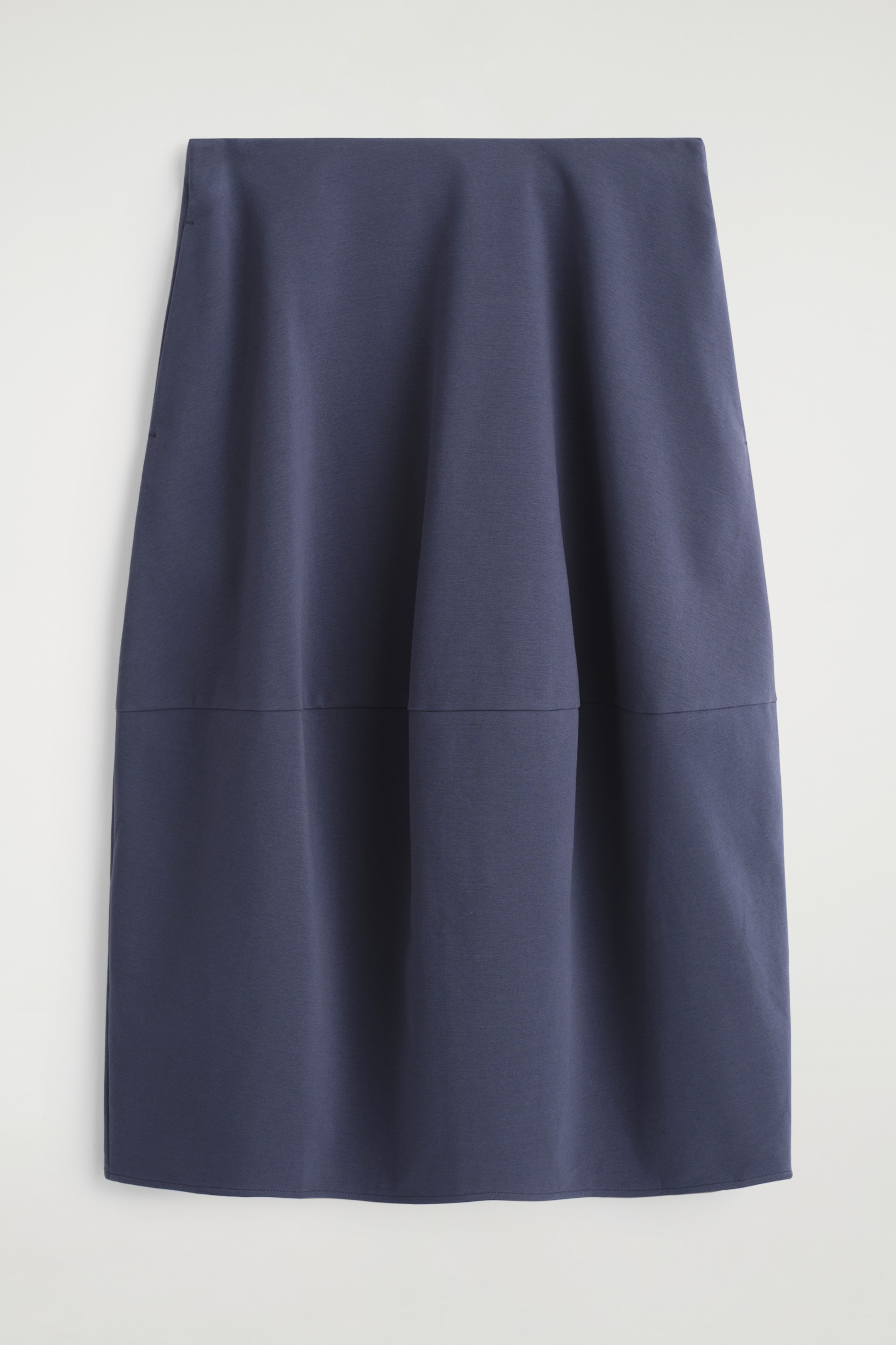 View larger image: A dark blue midi skirt is being displayed as a front view, laid flat. It is featuring a straight silhouette that gently flares towards the hem, subtle side-seam pockets, and a horizontal seam is visible across the lower third.