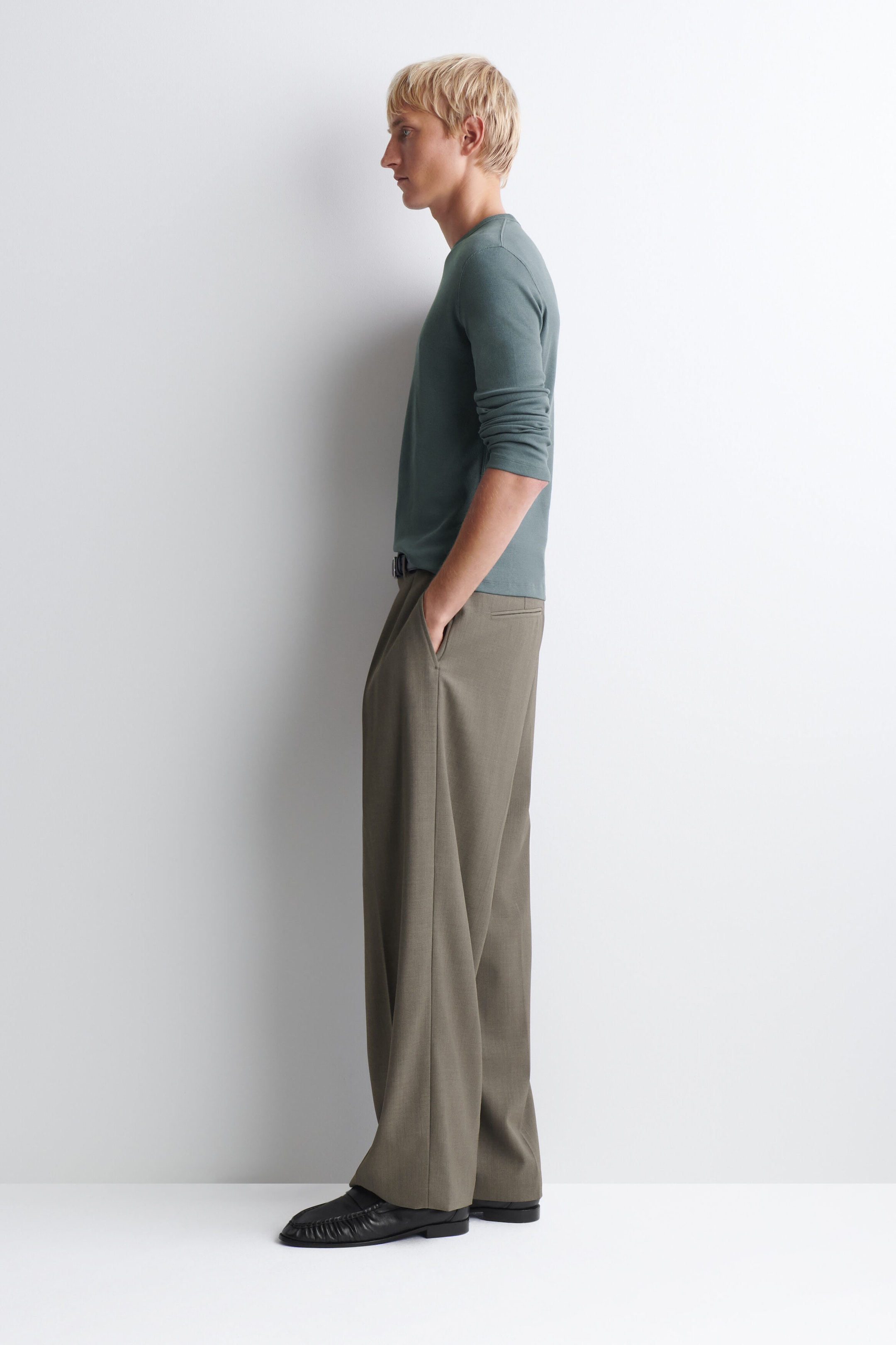 These wide-leg trousers in an olive-brown shade feature a relaxed, fluid drape and side slip pockets, shown in a left-facing side profile. They are styled with a muted green long-sleeve crewneck top and black leather loafers. These wide-leg trousers in an olive-brown shade feature a relaxed, fluid drape and side slip pockets, shown in a left-facing side profile. They are styled with a muted green long-sleeve crewneck top and black leather loafers.