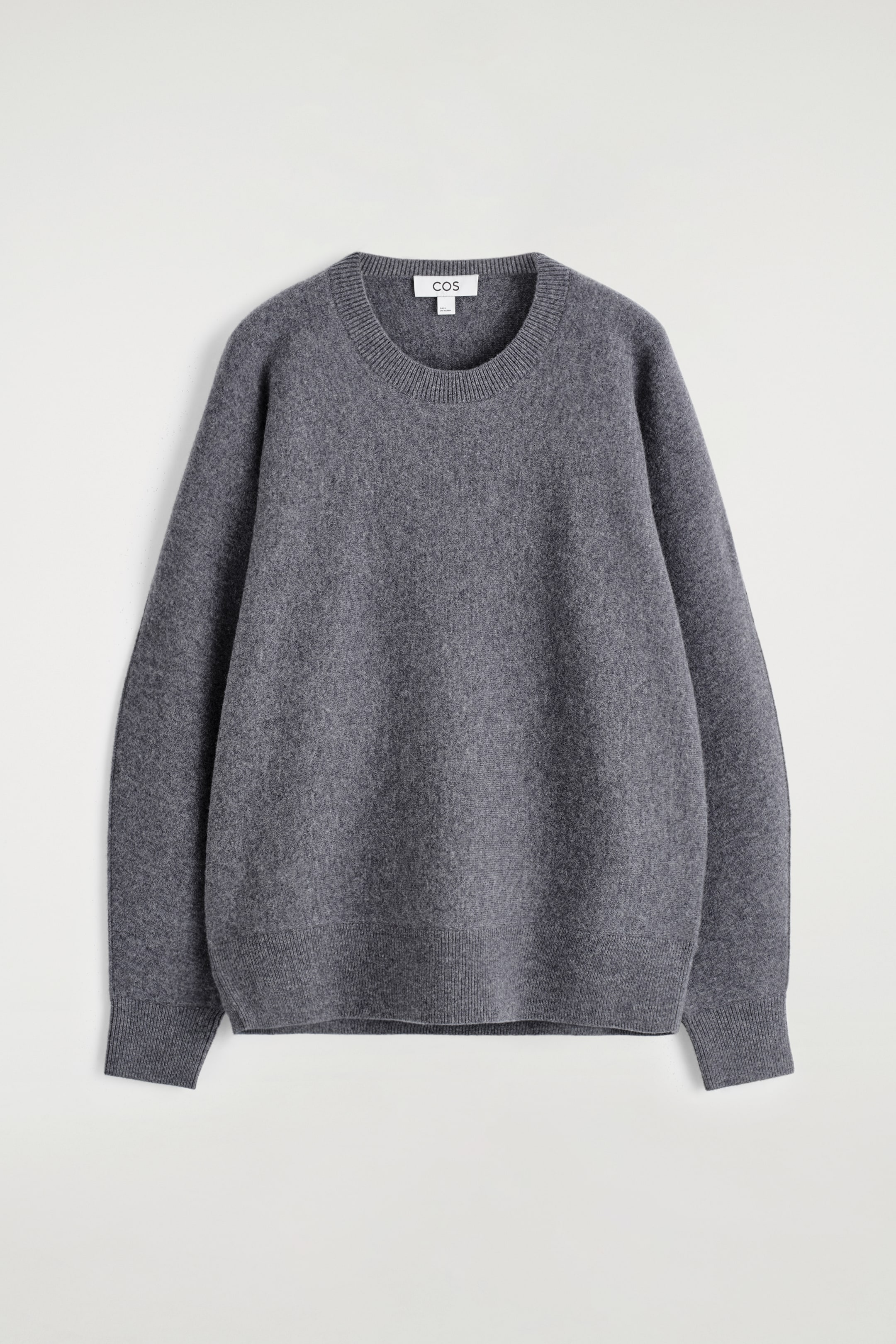 Grösseres Bild ansehen: Ein grauer Strickpullover ist vorne ausgelegt und zeigt eine entspannte Silhouette mit einem gerippten Rundhalsausschnitt, langen Ärmeln mit gerippten Bündchen und einem gerippten Saum, während das 'COS'-Markenetikett am Halsausschnitt sichtbar ist.