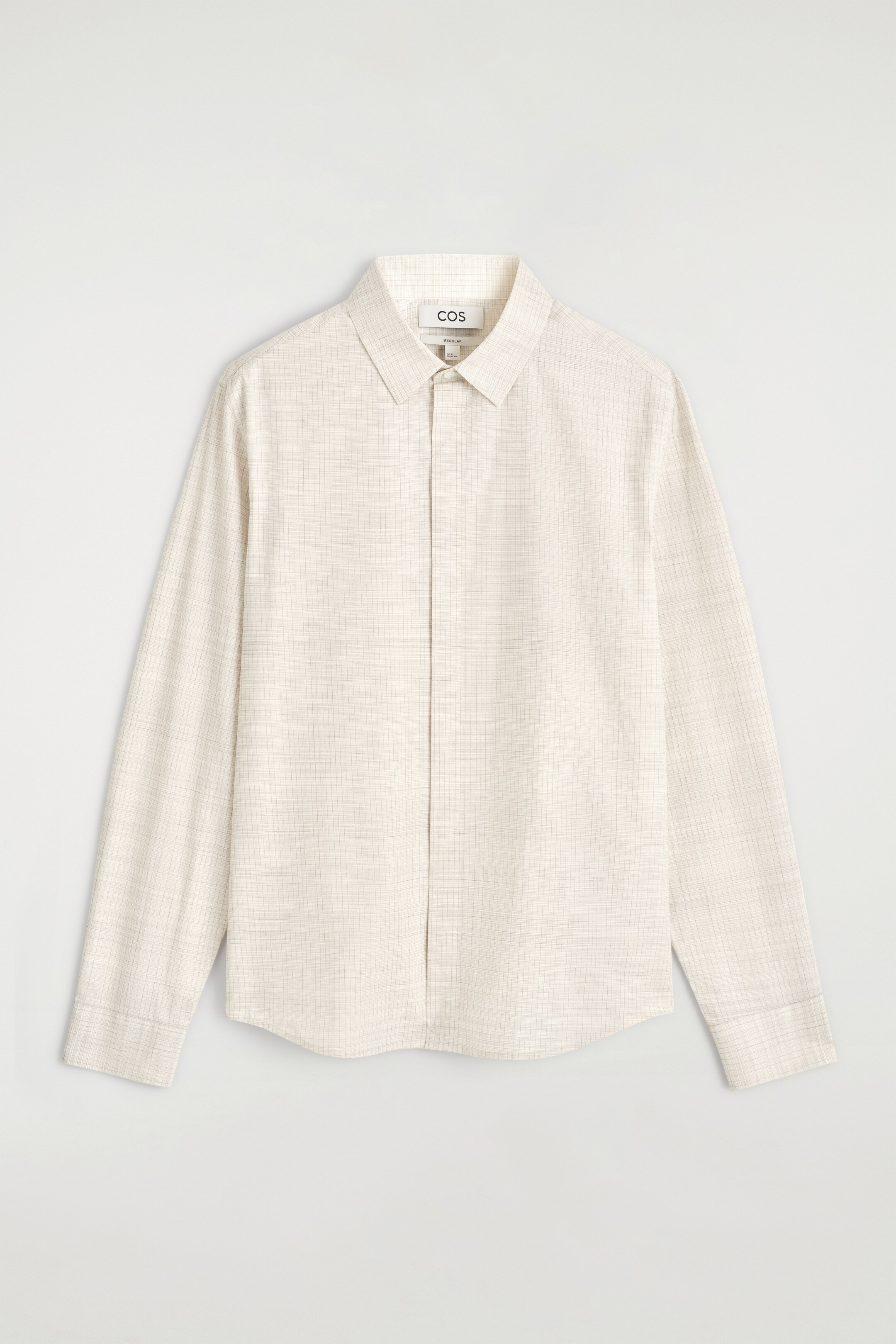 Agrandir l'image: Une chemise de couleur claire est présentée à l'avant, avec un motif à carreaux à fines lignes, un col pointu et une fermeture à boutons devant. Elle a des manches longues et une coupe décontractée.
