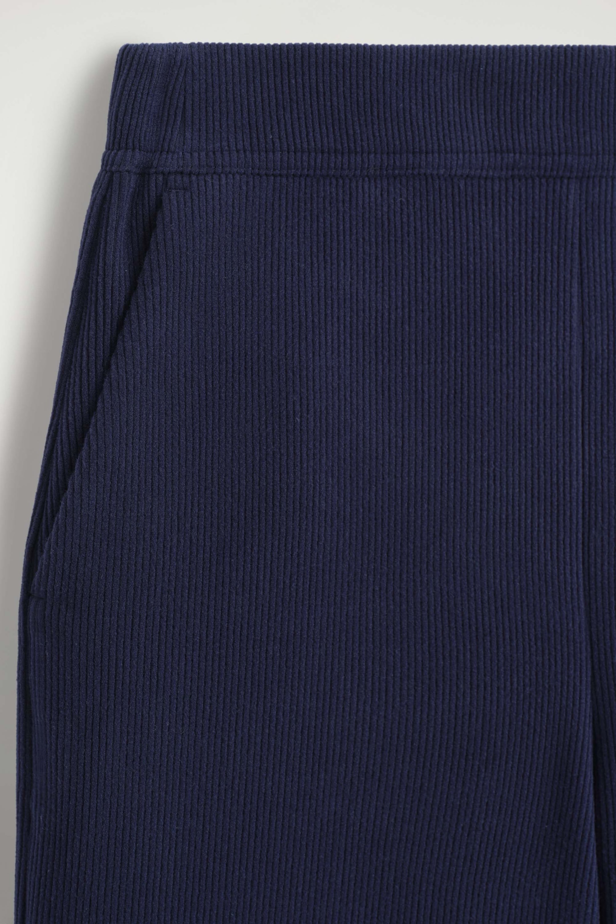 Les pantalons larges en jersey de velours côtelé sont montrés en gros plan de face, mettant en valeur la texture côtelée bleu marine foncé, une taille élastique plate et une poche latérale plaquée à gauche. Les pantalons larges en jersey de velours côtelé sont montrés en gros plan de face, mettant en valeur la texture côtelée bleu marine foncé, une taille élastique plate et une poche latérale plaquée à gauche.