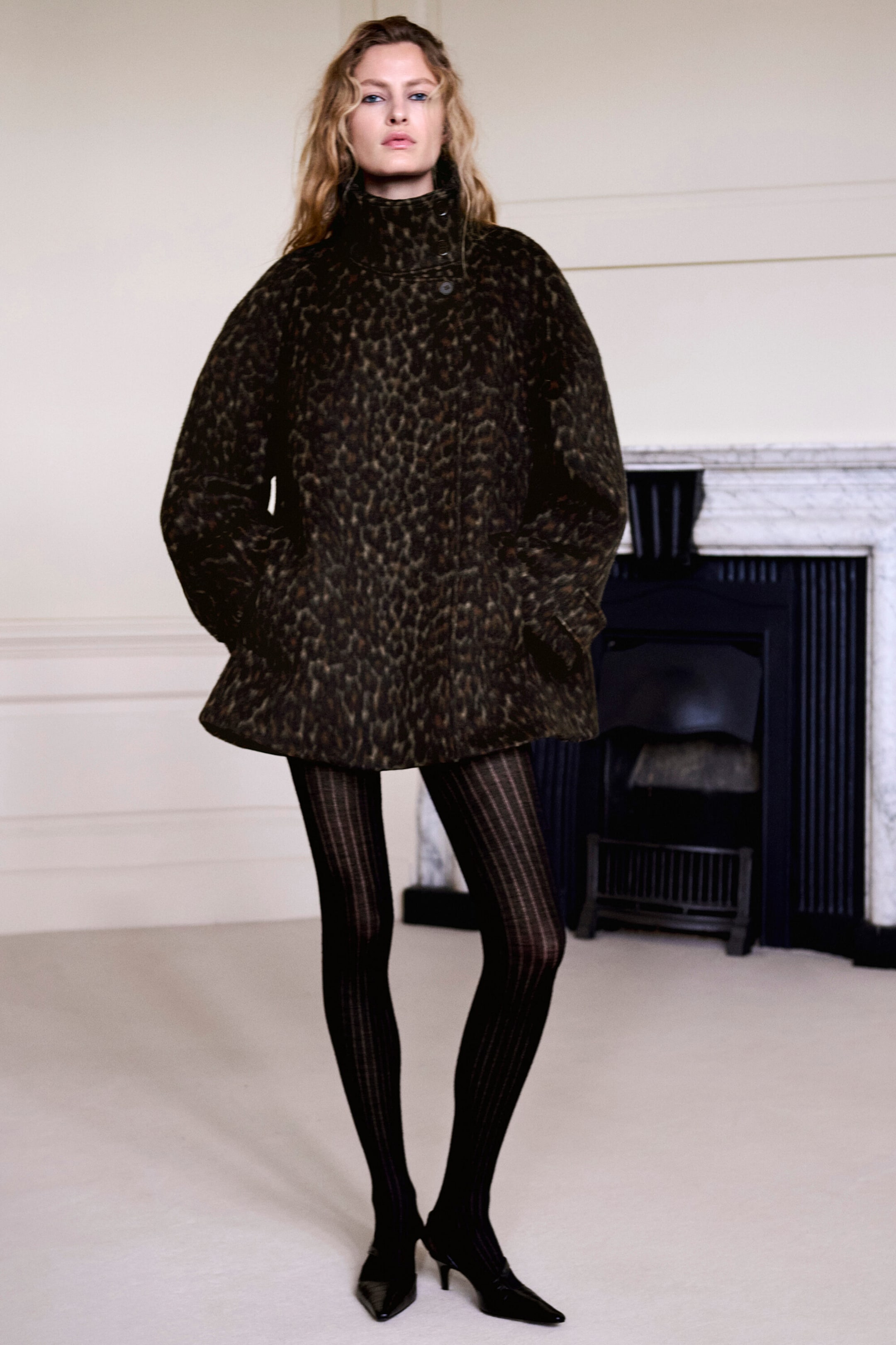 Der Mantel mit Leopardenmuster ist von vorne zu sehen und präsentiert eine übergroße, ausgestellte Silhouette mit hohem Trichterausschnitt und weiten Ärmeln. Er wird mit transparenten schwarzen Rippstrumpfhosen und schwarzen Kitten Heels mit spitzer Zehenpartie kombiniert. Der Mantel mit Leopardenmuster ist von vorne zu sehen und präsentiert eine übergroße, ausgestellte Silhouette mit hohem Trichterausschnitt und weiten Ärmeln. Er wird mit transparenten schwarzen Rippstrumpfhosen und schwarzen Kitten Heels mit spitzer Zehenpartie kombiniert.