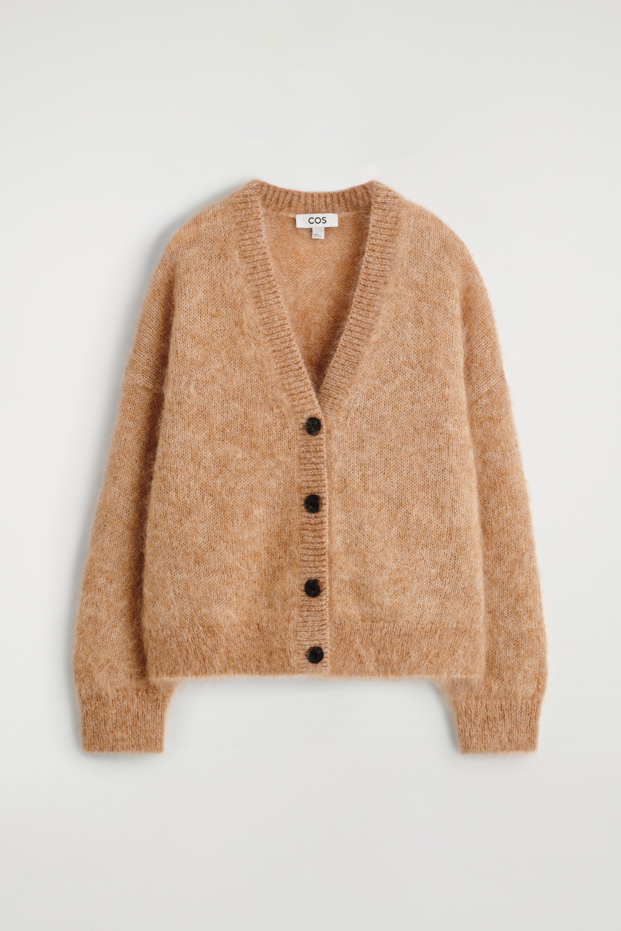 Grösseres Bild ansehen: Ein locker sitzender Cardigan wird von vorne gezeigt, gestrickt in einer Kamel-Mélange-Farbe mit einer sichtbar flauschigen Textur. Er verfügt über einen gerippten V-Ausschnitt, fünf dunkle Knöpfe in der Mitte vorne sowie gerippte Bündchen und einen gerippten Saum.