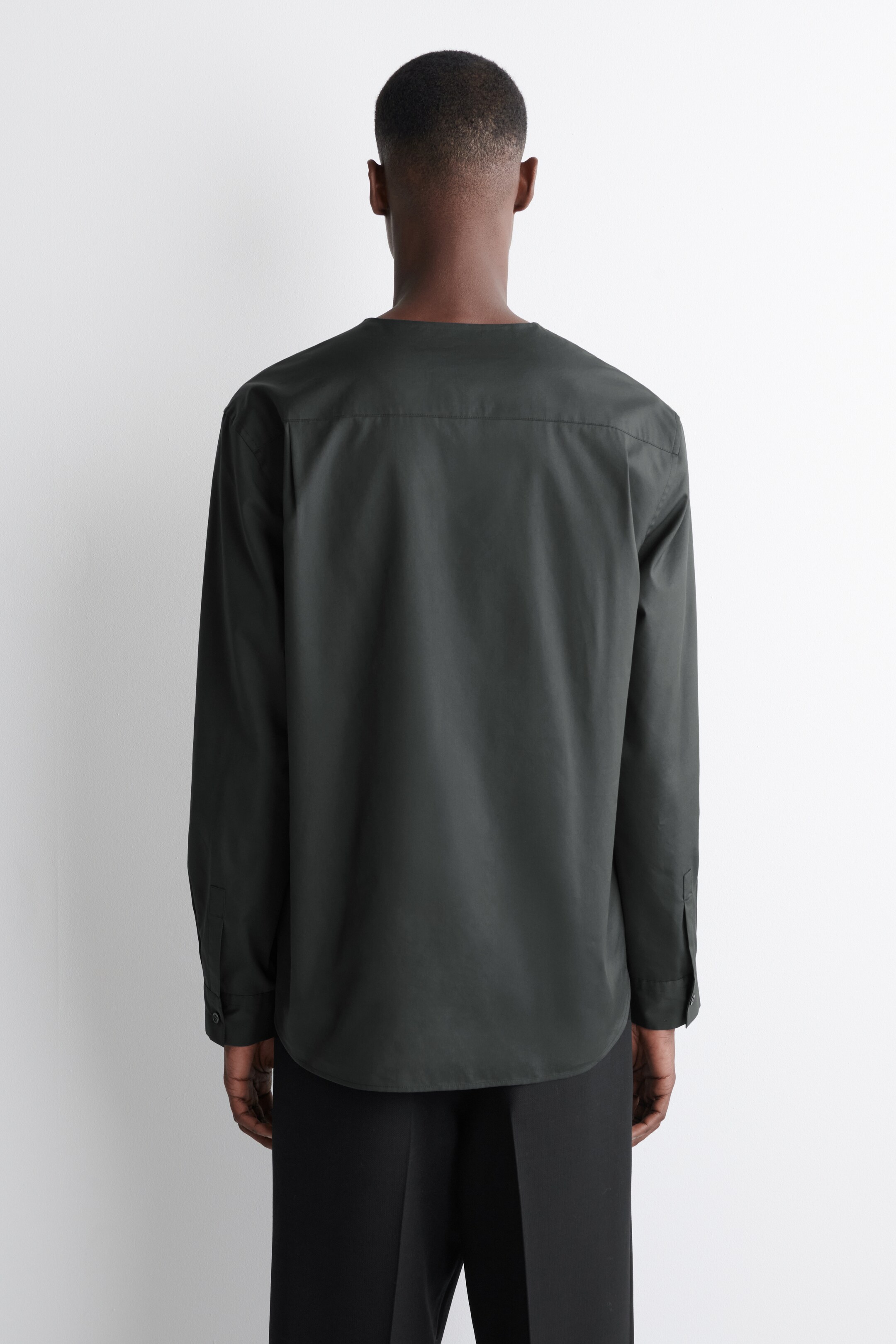 Ver imagen más grande: Una camisa gris oscuro de manga larga está de espalda, con un escote sin cuello y un canesú en la parte superior de la espalda. Está diseñada con mangas largas, puños abotonados y un dobladillo redondeado.