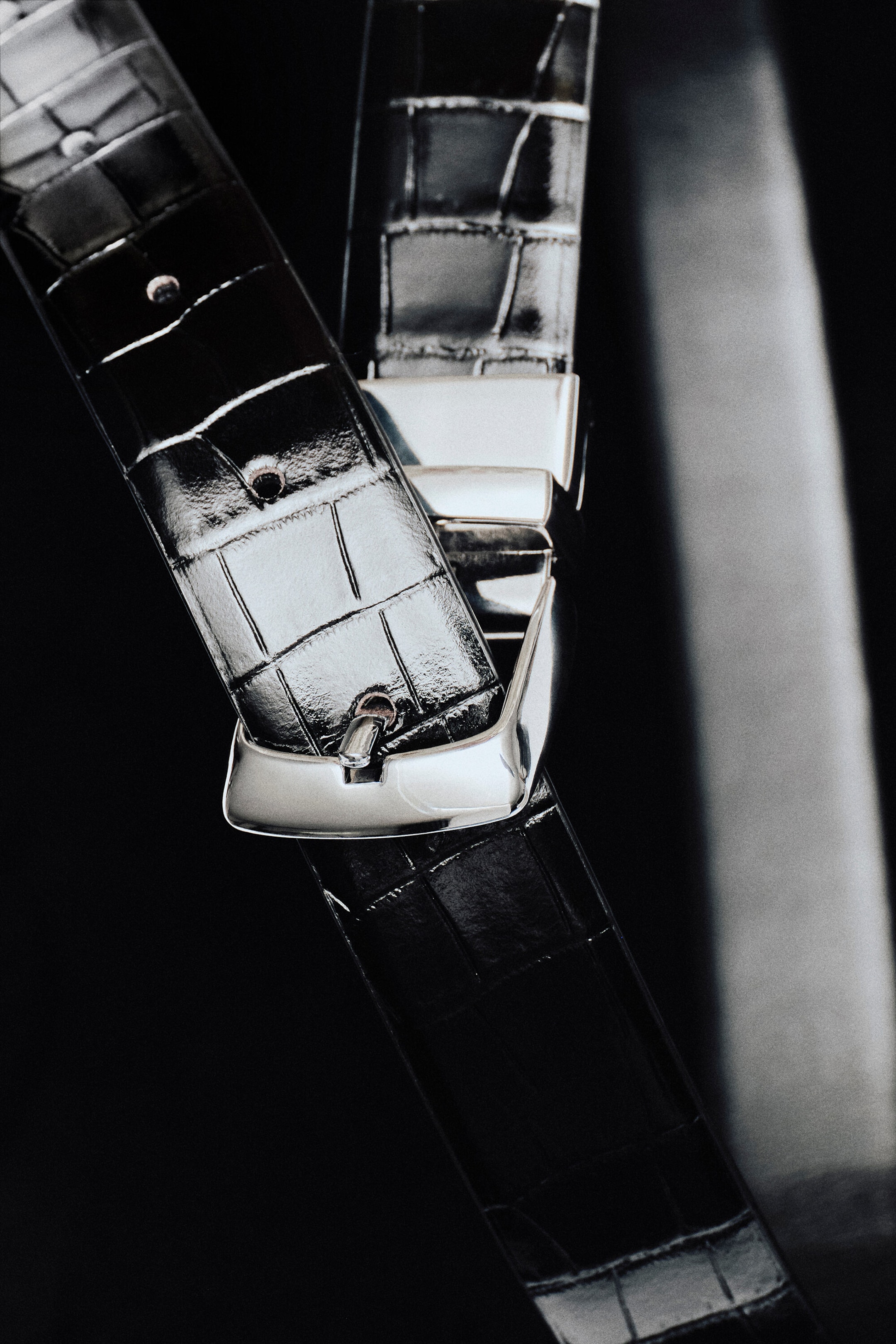 A reversible leather belt is shown with a black, croc-embossed leather strap featuring a glossy finish. The strap loops through a polished silver-tone metal buckle, highlighting the textured pattern and pre-punched adjustment holes. A reversible leather belt is shown with a black, croc-embossed leather strap featuring a glossy finish. The strap loops through a polished silver-tone metal buckle, highlighting the textured pattern and pre-punched adjustment holes.