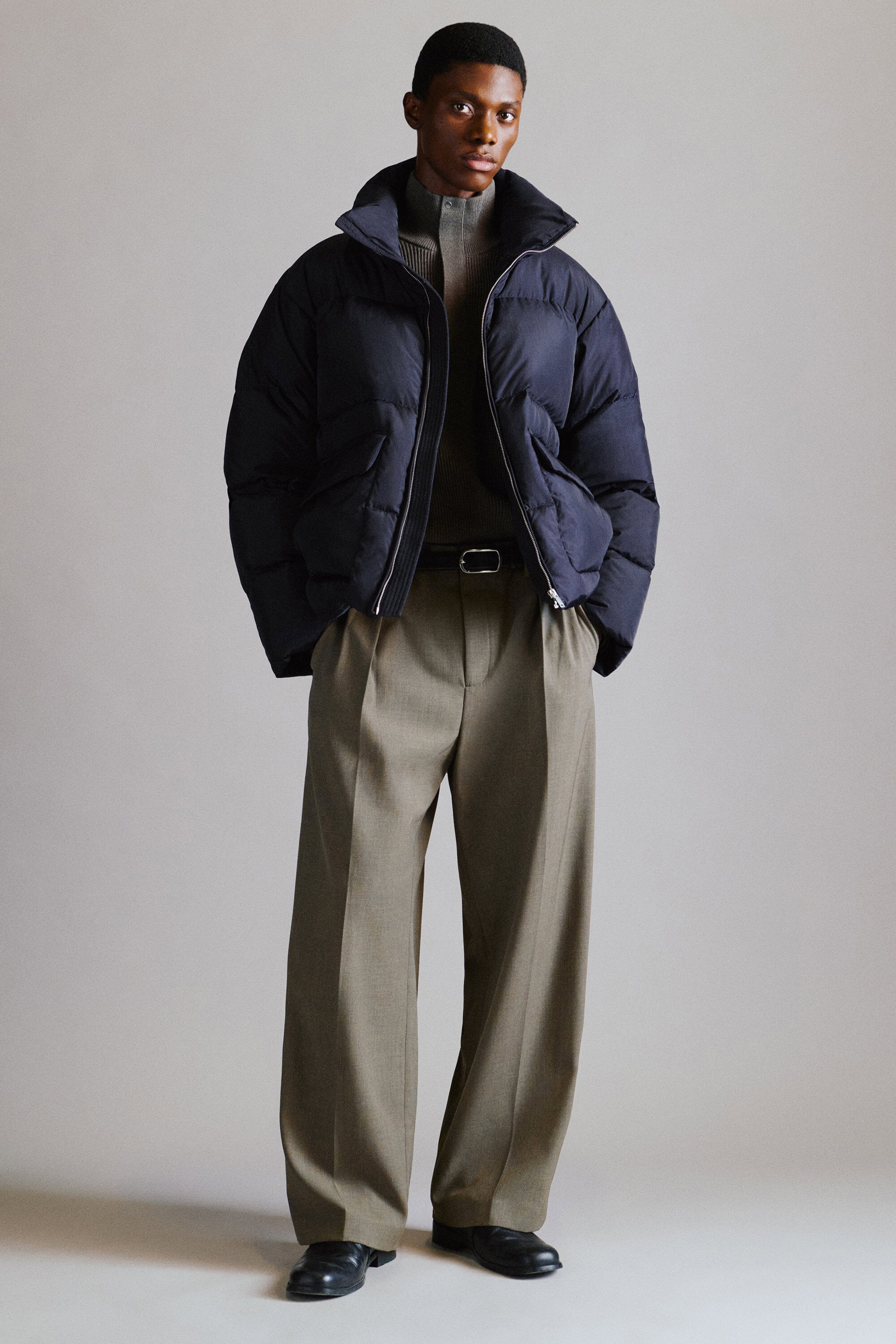The navy blue funnel-neck nylon down puffer jacket is styled open, featuring a quilted construction and a high funnel neck. It is paired with taupe wool-blend relaxed-fit wide-leg trousers that feature front pleats and a loose, draped silhouette, shown from a front-facing angle. The navy blue funnel-neck nylon down puffer jacket is styled open, featuring a quilted construction and a high funnel neck. It is paired with taupe wool-blend relaxed-fit wide-leg trousers that feature front pleats and a loose, draped silhouette, shown from a front-facing angle.